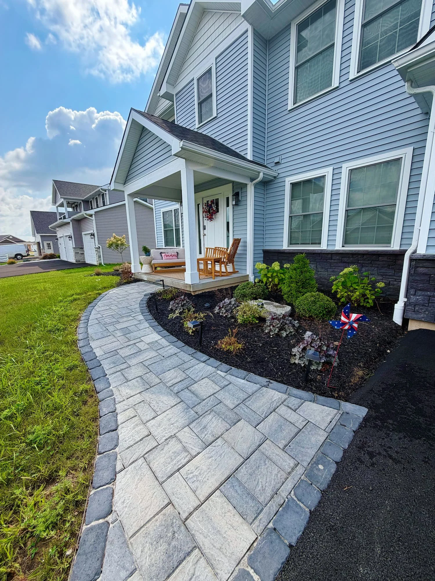 Front yard landscaping with a curved paver walkway, planting beds, and fresh mulch in Central NY.