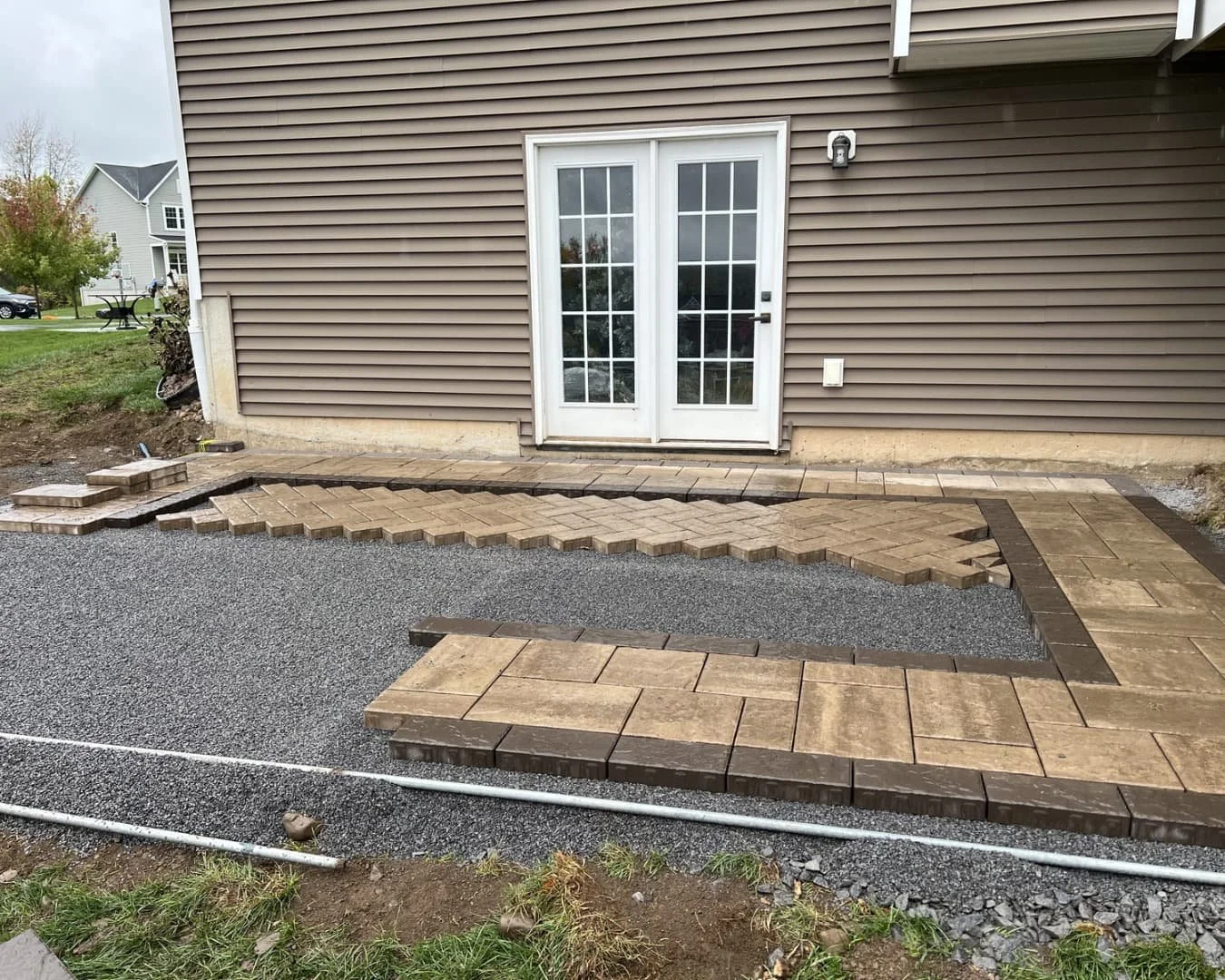 Backyard hardscape work in progress beside a home in Upstate New York with patio base visible.