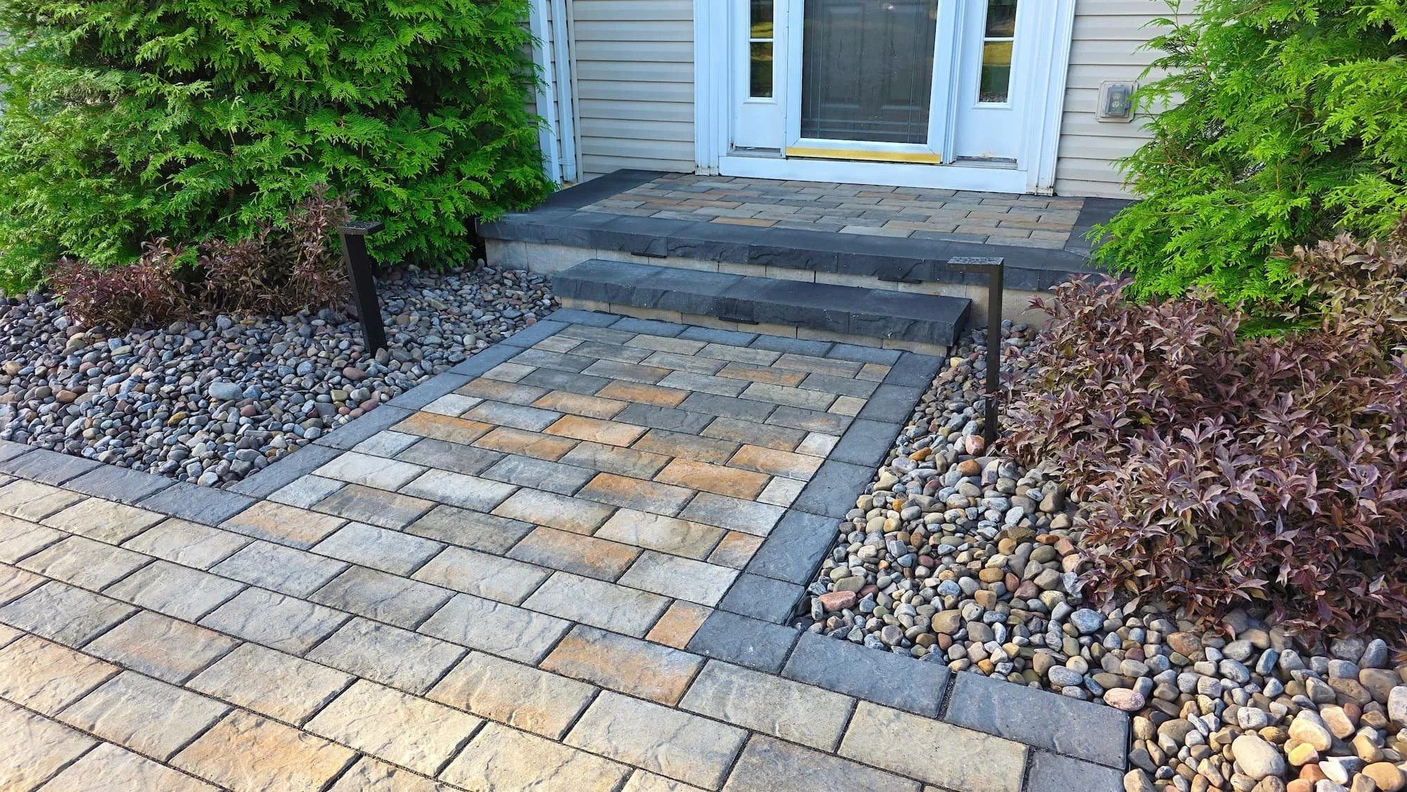 Warm outdoor lighting highlighting a custom paver patio and entry step at a Central NY home.
