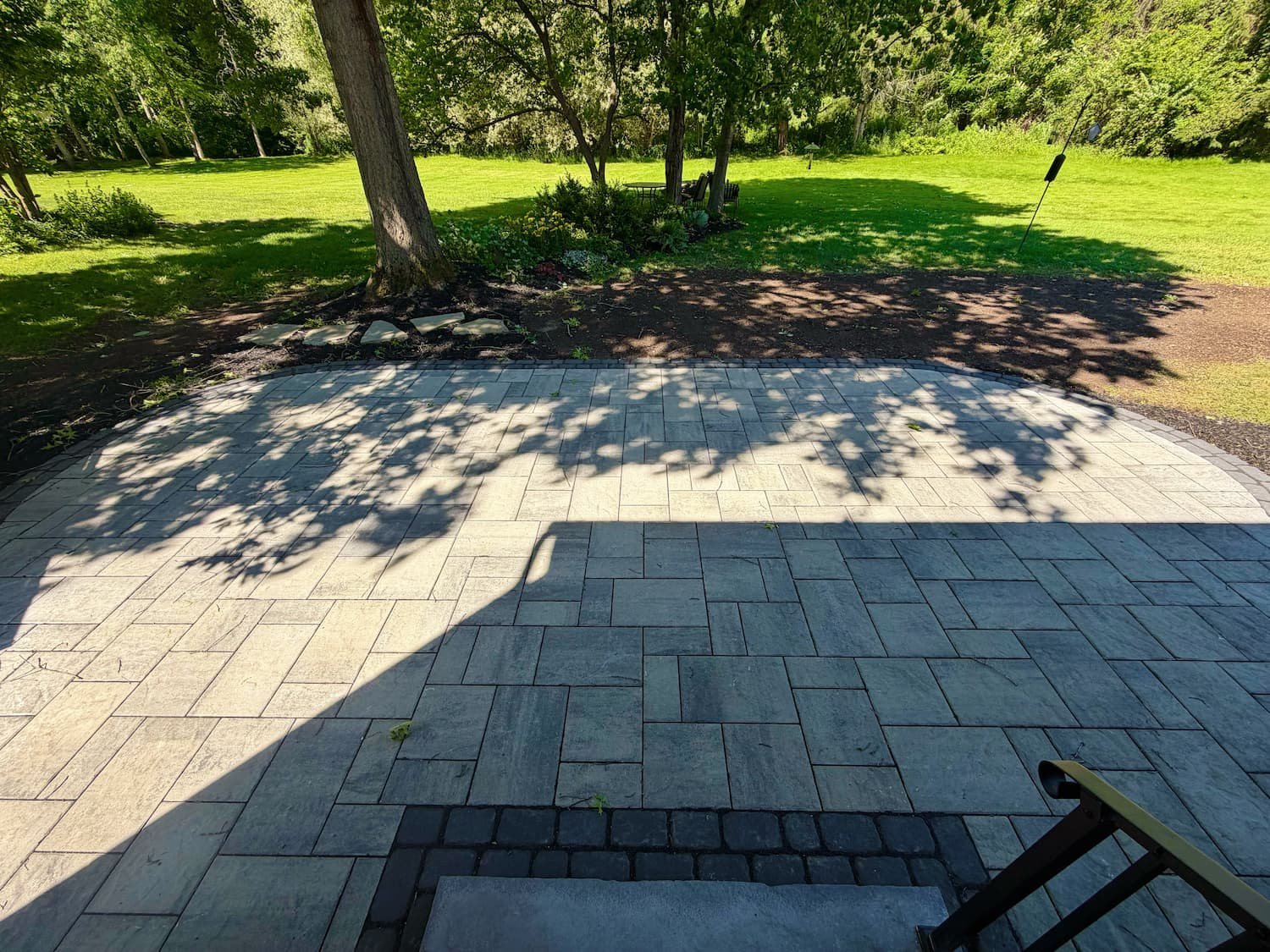 Custom hardscape patio surrounded by mature trees and landscaping at a Central New York home.