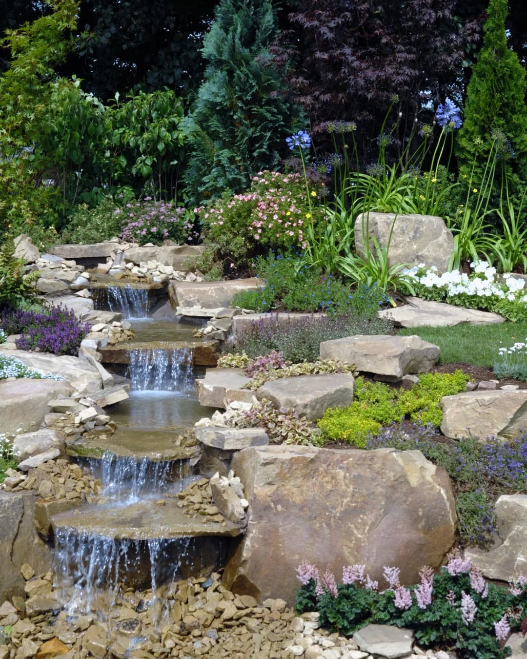 Water feature inspiration with a tiered rock fountain surrounded by natural stone and planting.