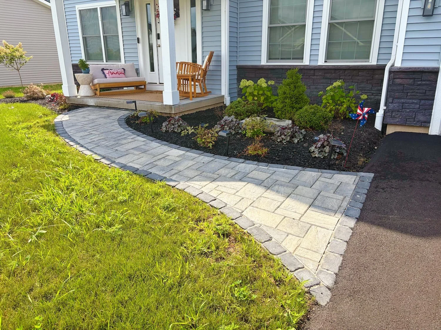 Finished front entry with a curved paver walkway, landscaped planting beds, shrubs, and fresh mulch in Central NY.