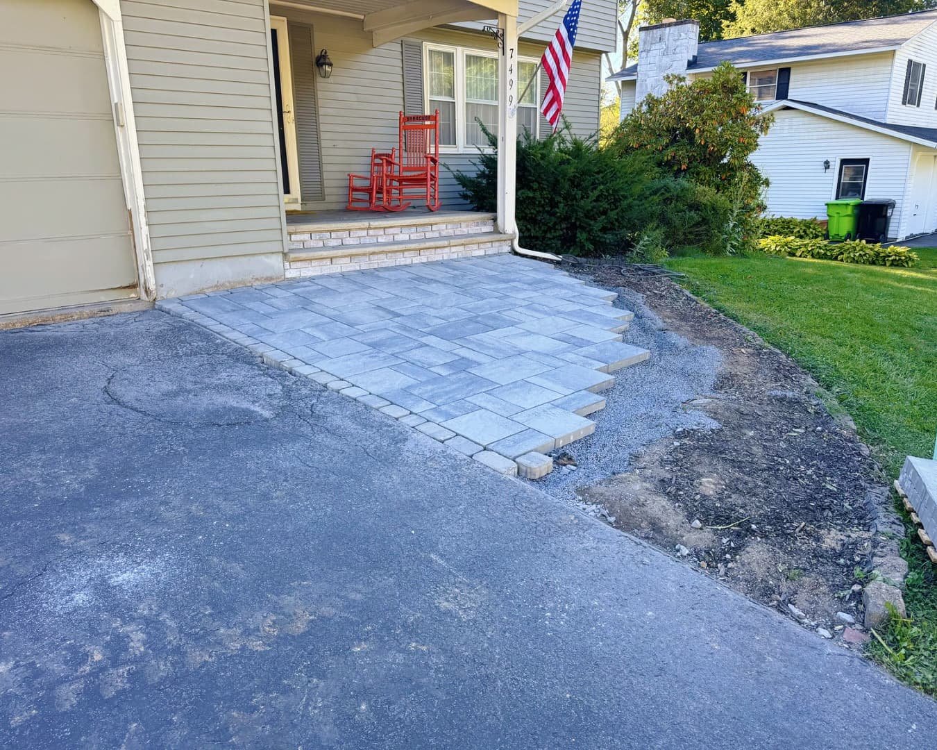 Front hardscape overview at a Central New York home showing a finished paver patio with curved edging and entry access.