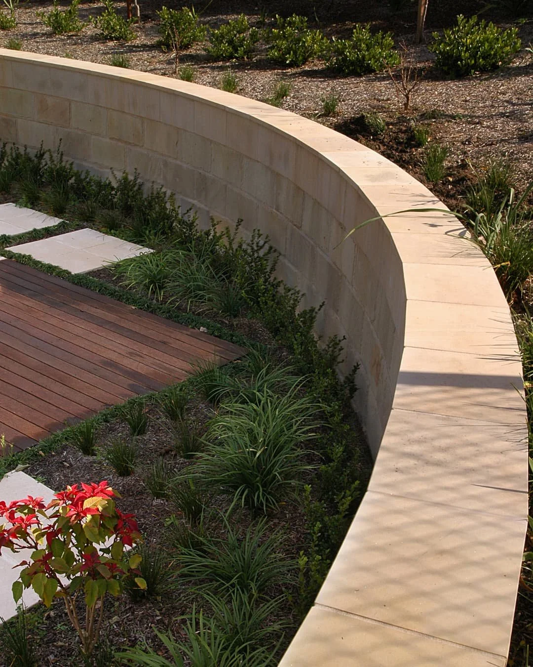 Curved retaining wall inspiration with layered stone and planting beds beside a lawn area.