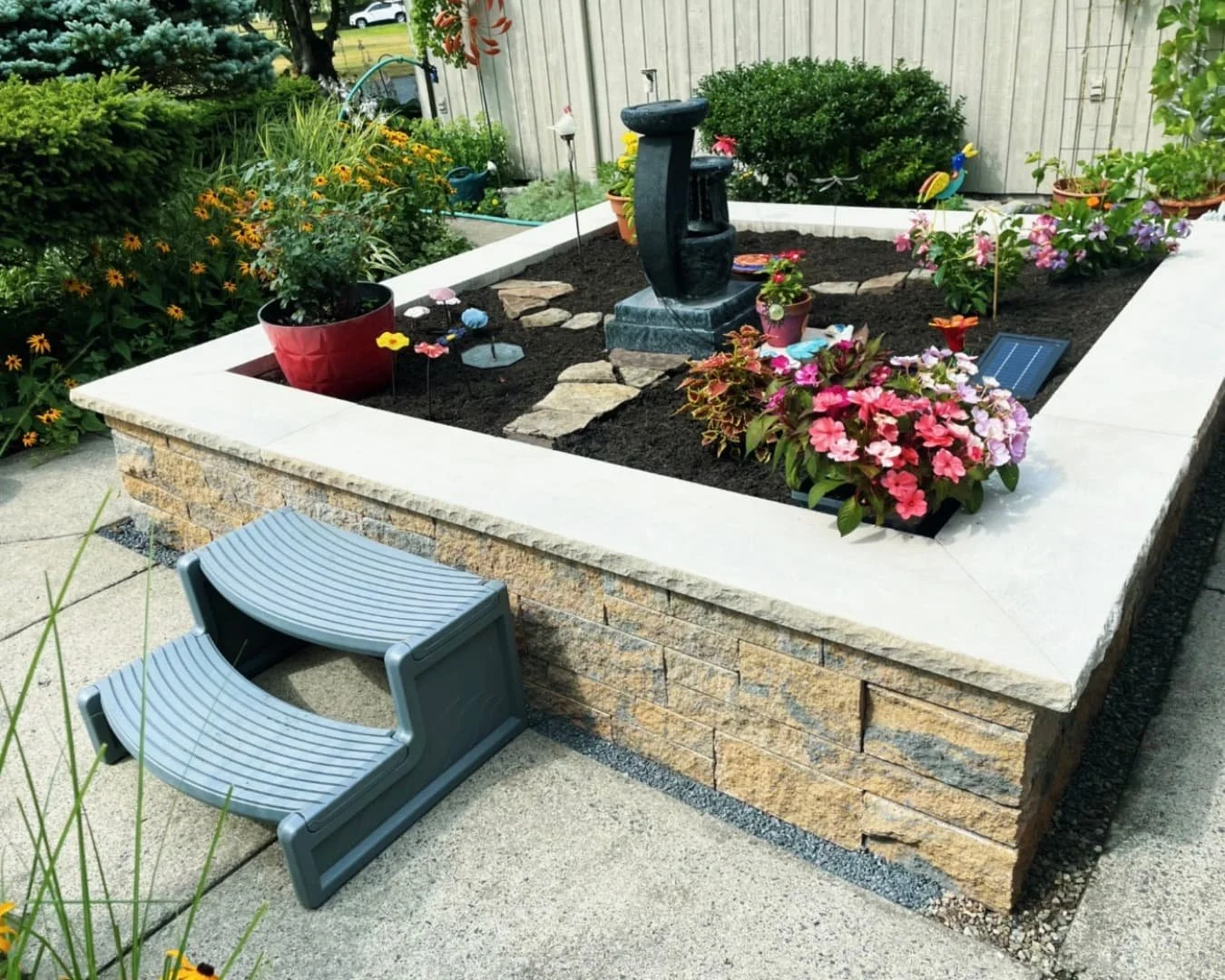 Front yard raised planter at a Skaneateles, NY home with flowers, clean edging, and a finished outdoor feature.
