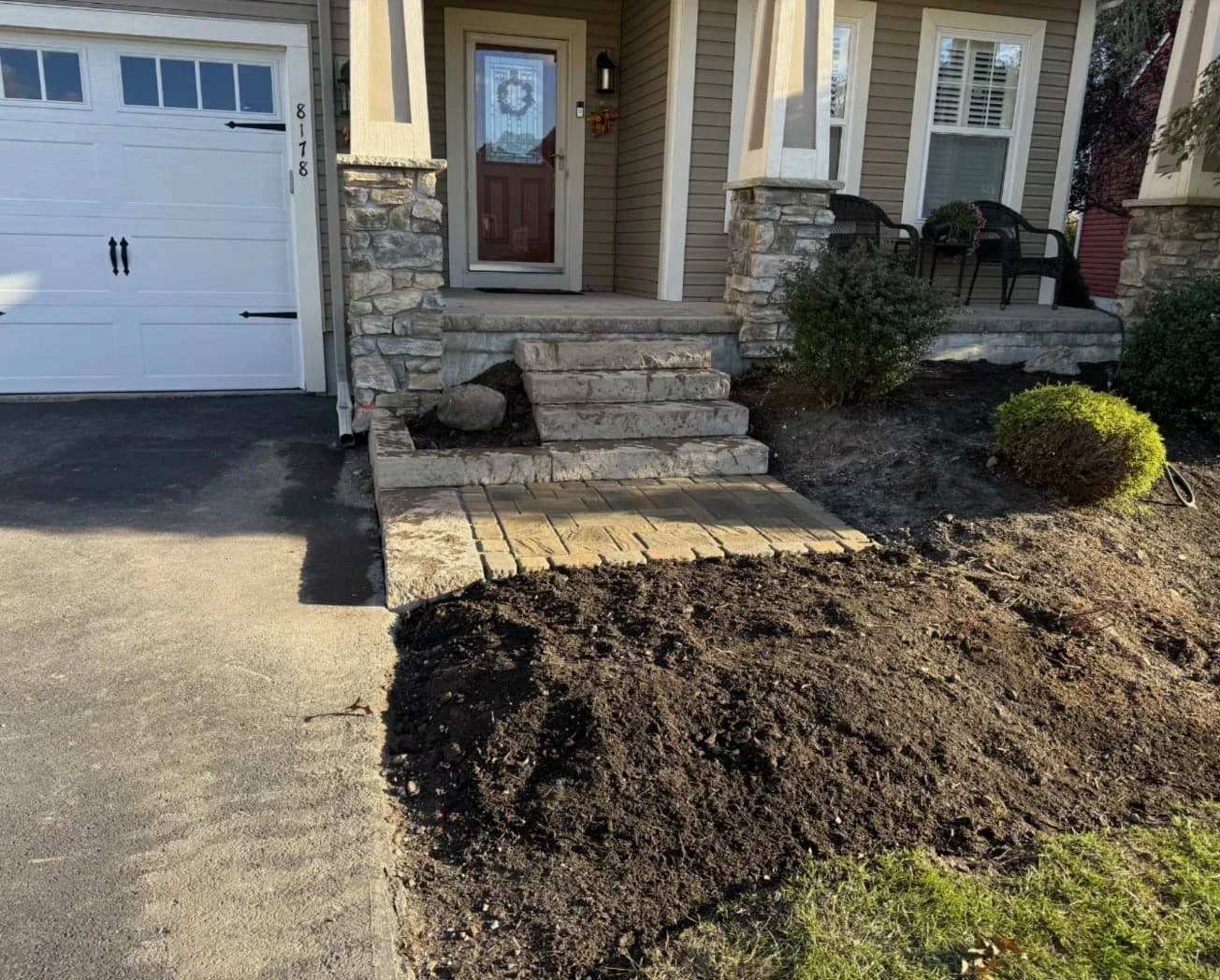 Stone front steps and entry landing at a Marcellus, NY home with natural stone pillars and fresh mulch beds.
