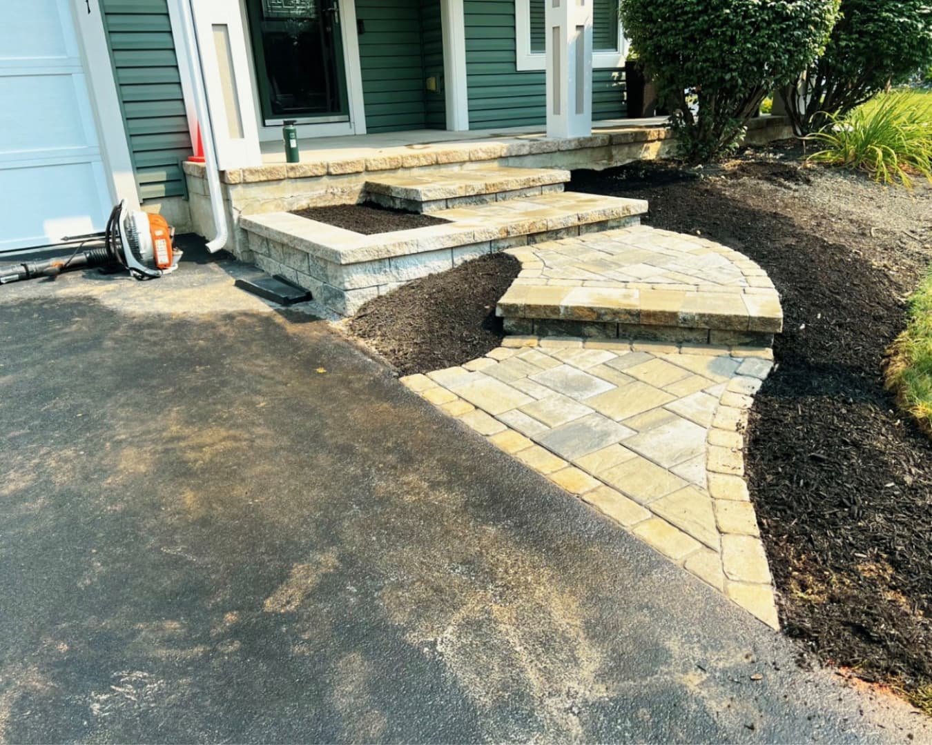 Front entry hardscape construction at a Manlius, NY home with curved steps, fresh excavation, and stone materials on site.