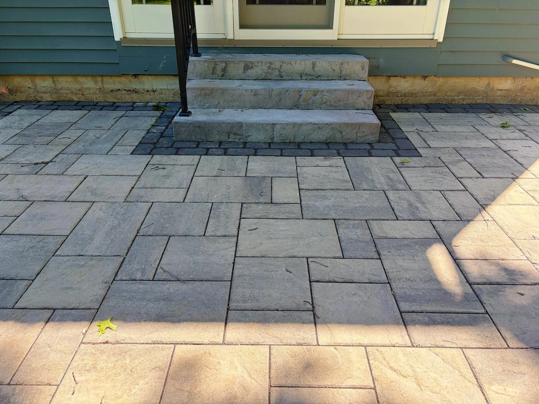 Detailed view of custom paver patio installation with stone steps leading to the home in Central New York.