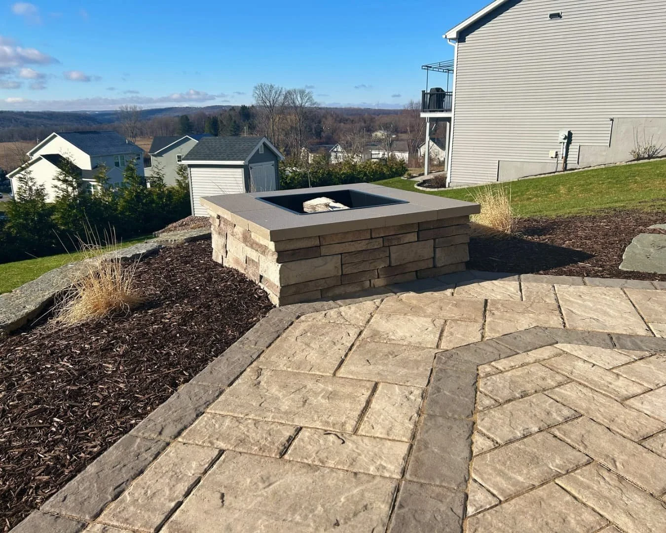 Landscape bed and fire feature detail completed by Pines and Pavers in Lysander, New York.
