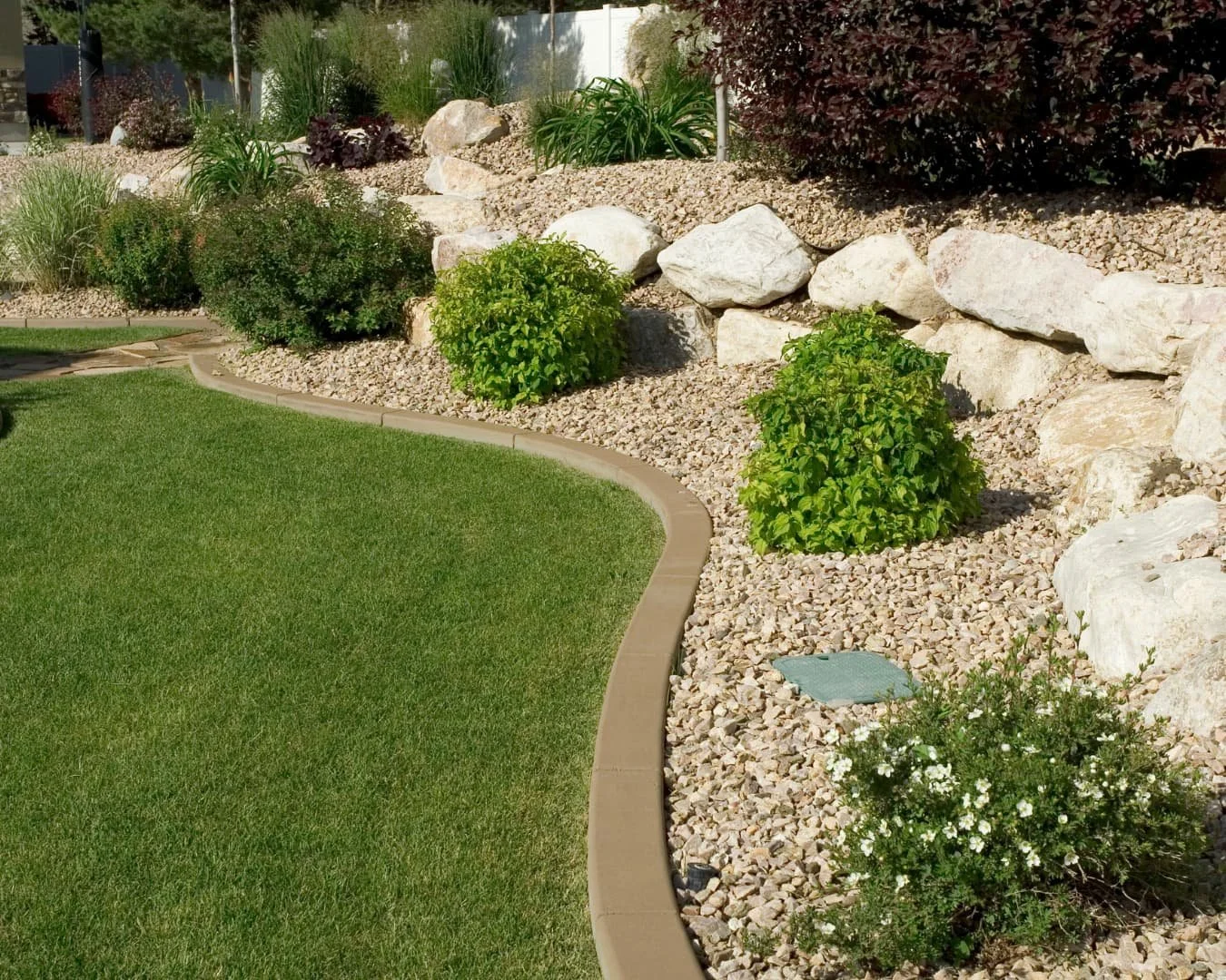 Layered landscaping inspiration with a curved bed edge, rock border, and mixed shrub planting beside the lawn.