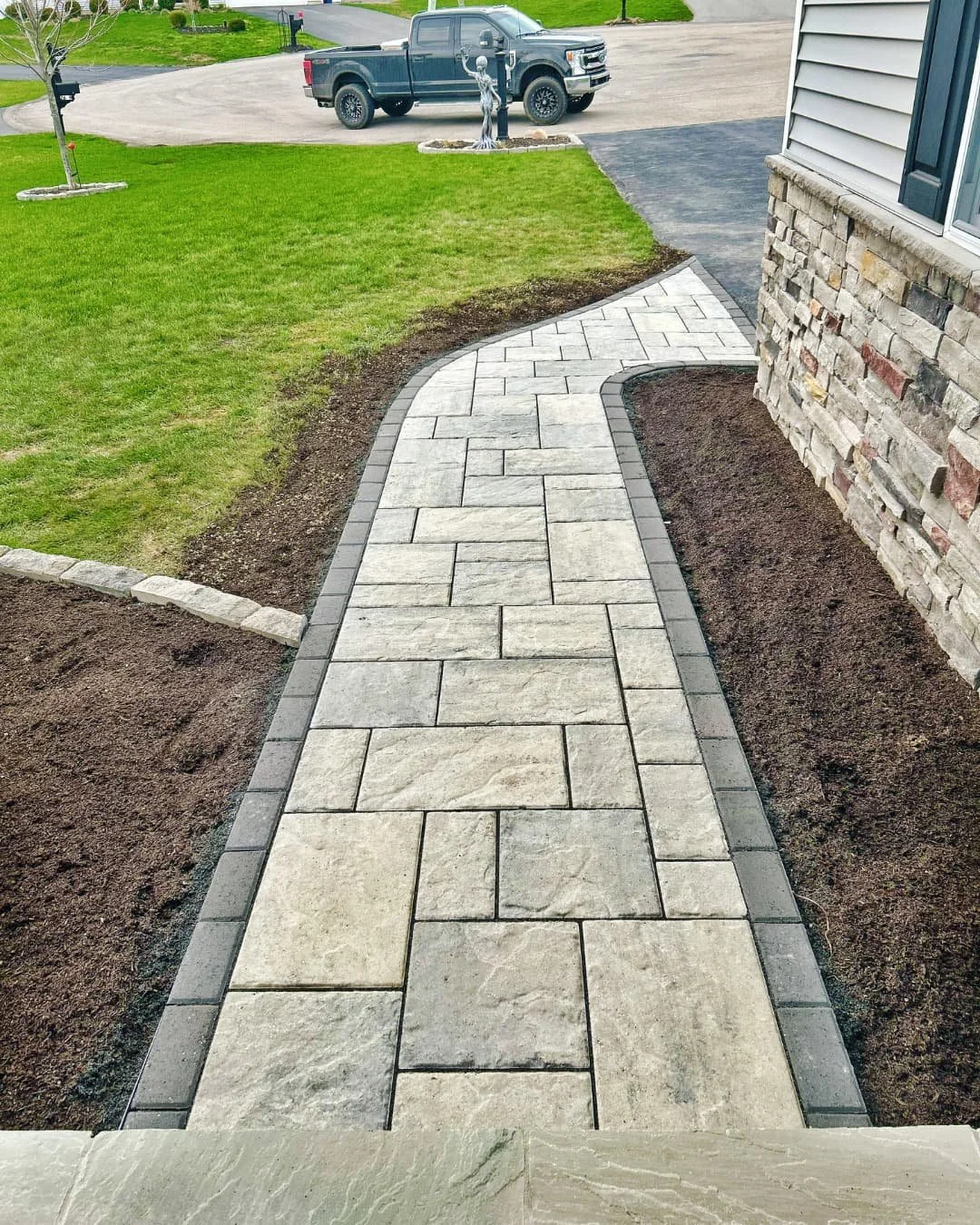     Curved front sidewalk beside the driveway with fresh landscape beds and clean edging.