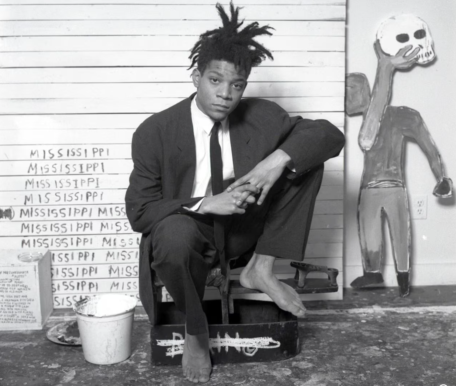 Jean Michel Basquiat sitting in front of his painting in a suit