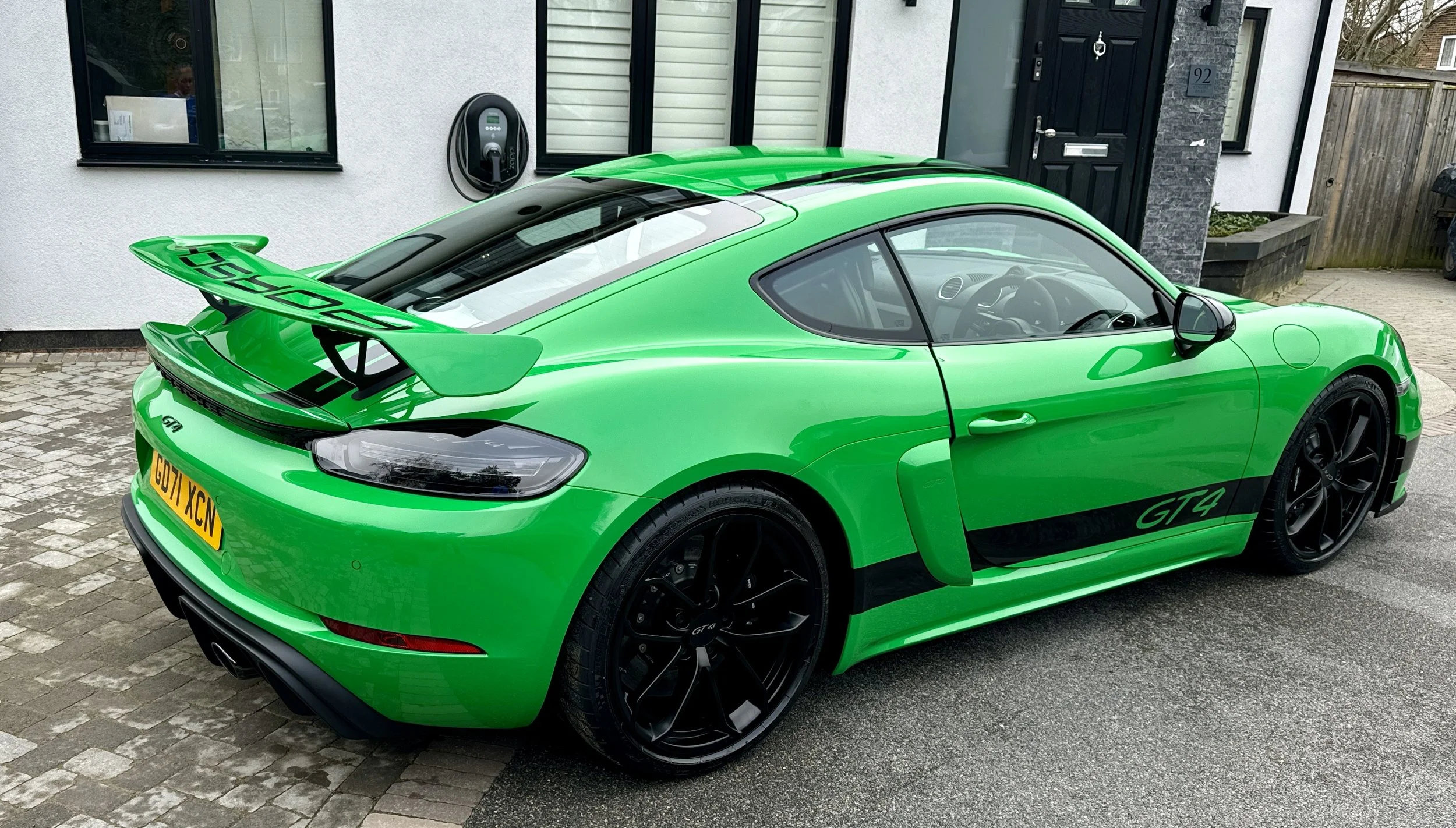 A bright green Porsche 718 Cayman GT4 parked outside a house on a cobblestone driveway.