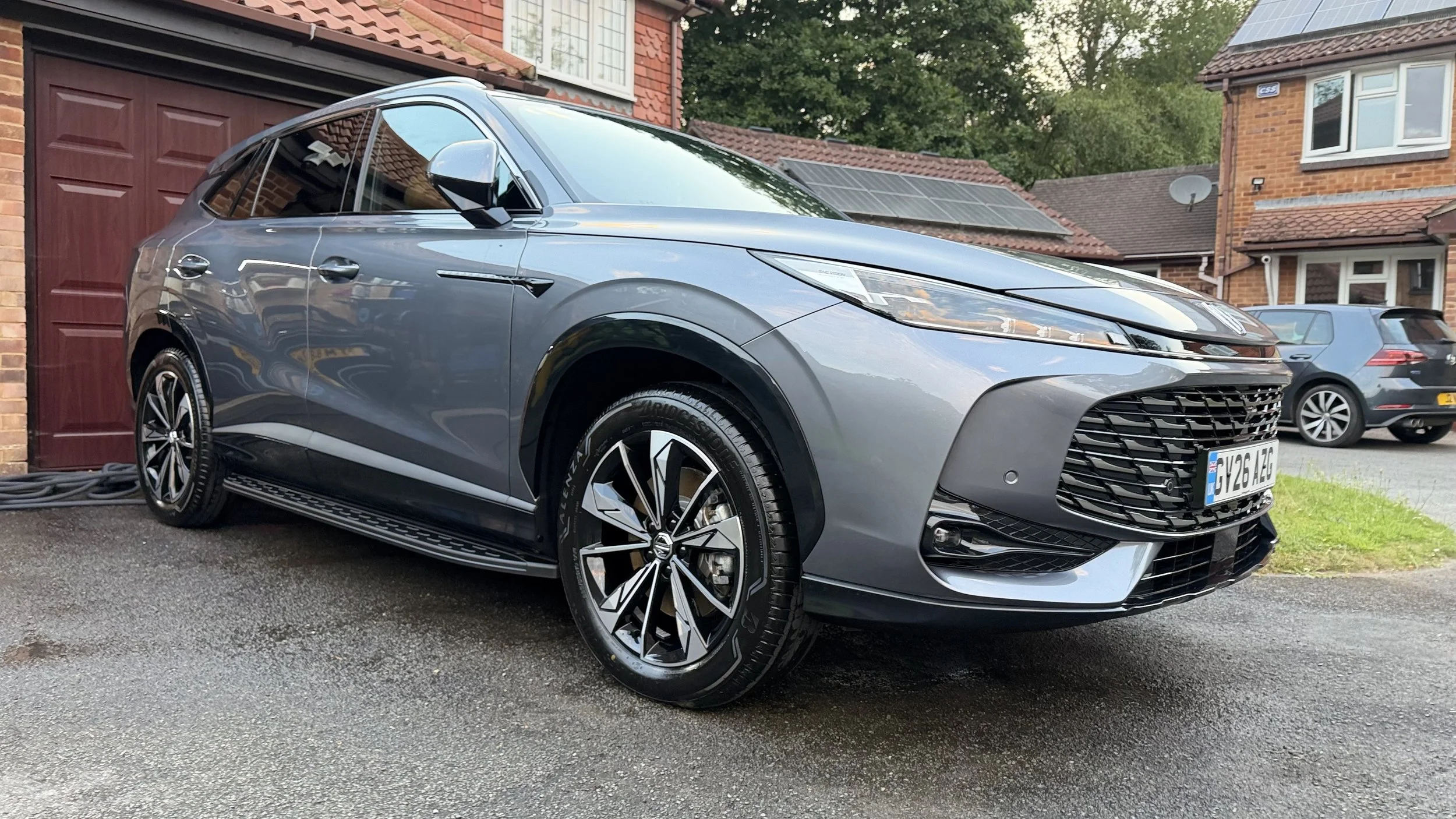A grey electric Honda HR-V parked outside a house with a red garage door, with solar panels on the roof, on a driveway with two other cars parked nearby. D Car Detailing Mobile Detailer In Kent