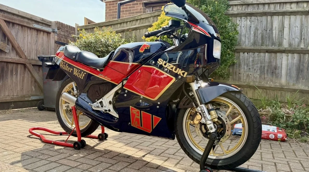 A vintage Suzuki motorcycle with a Walter Wolf racing livery parked on a brick driveway, supported by a red stand.