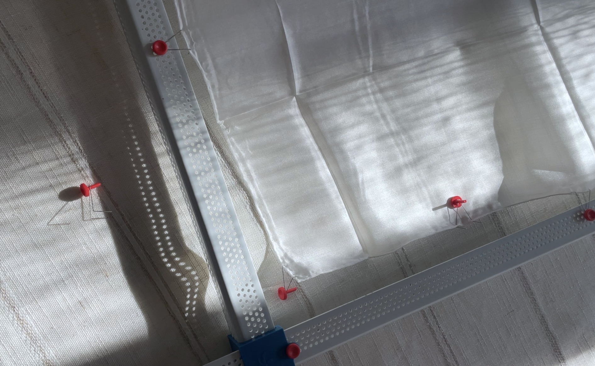 A partial view of a metal frame and red push pins securing silk. First step in the batik creation process.