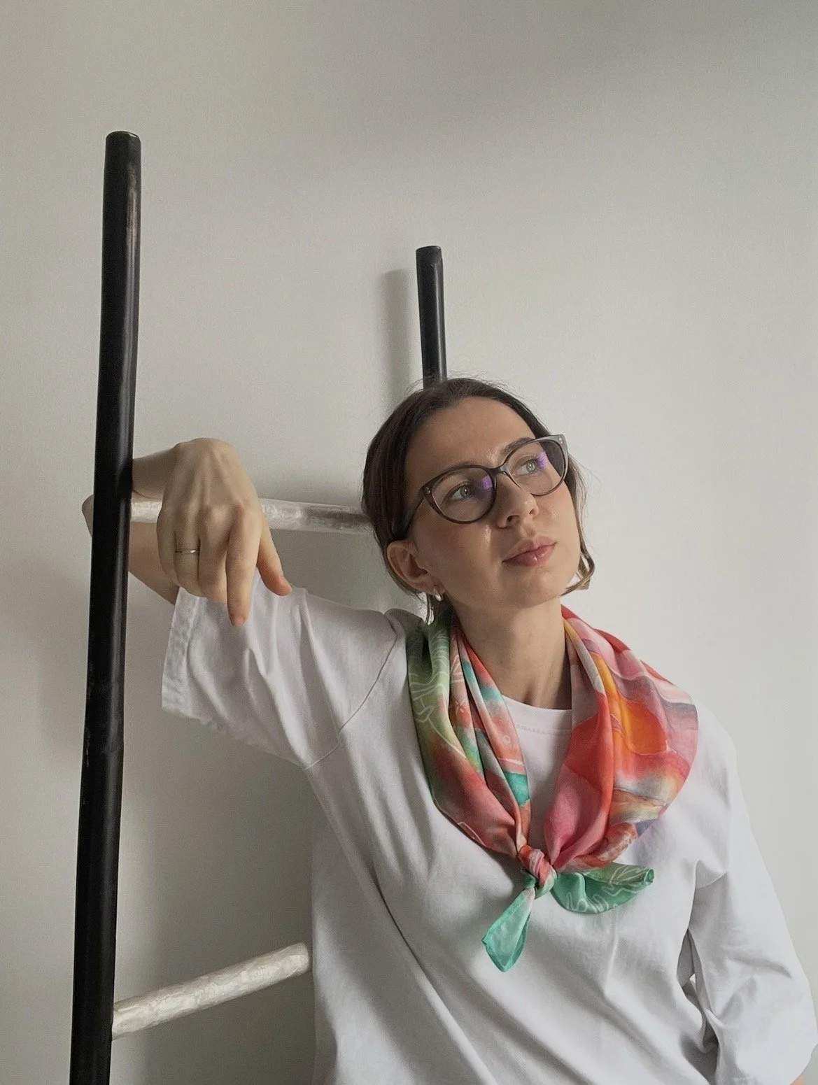 A woman with glasses and a colourful silk scarf near a wall.
