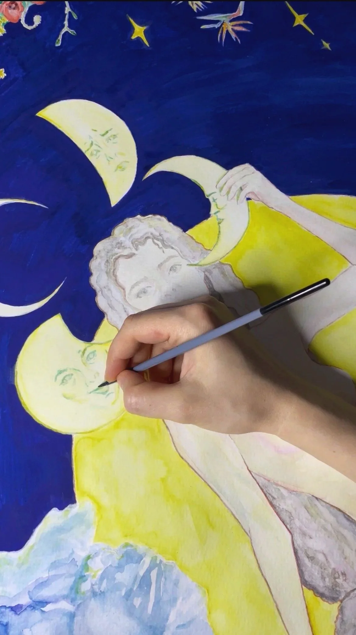 Artist painting a fantasy scene of a woman with crescent moon face, surrounded by moons, stars, clouds, and night sky.