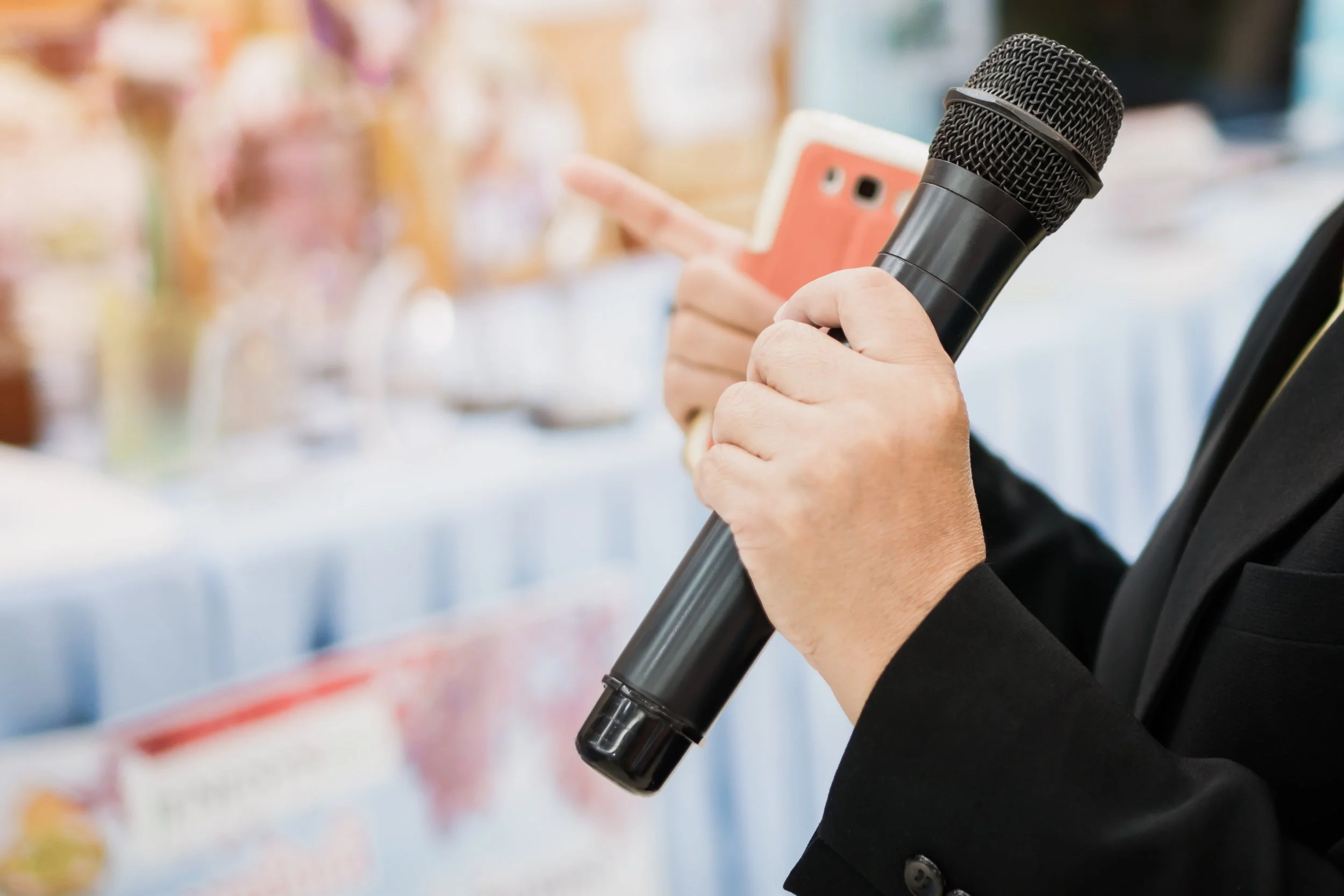 Person holding a black microphone and a pink smartphone in a setting that appears to be a store or event space.