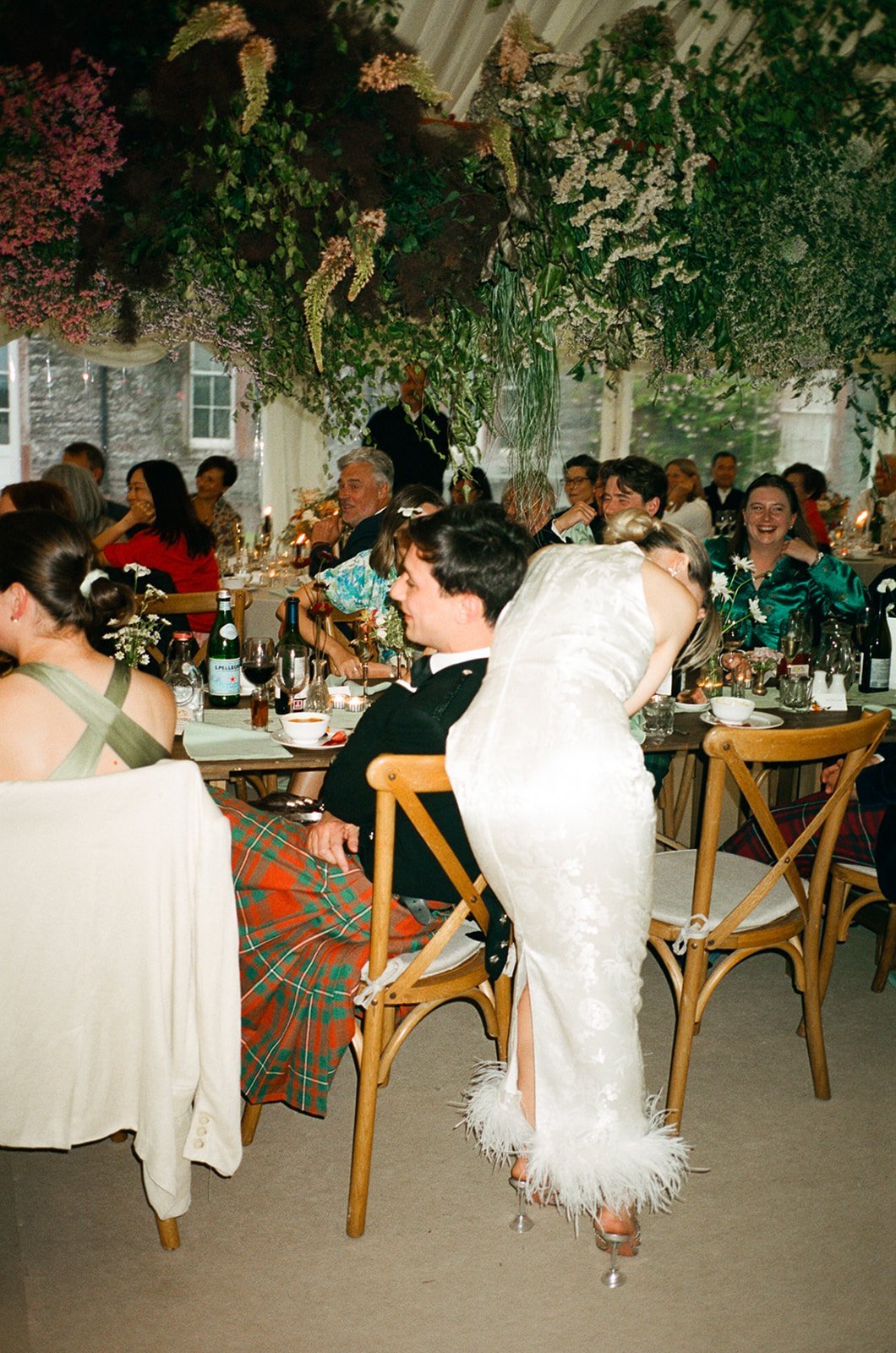 Bride and Groom on 35mm Film at Marquee wedding in Scotland. Bride wear dress with feather detail. Groom wears kilt.