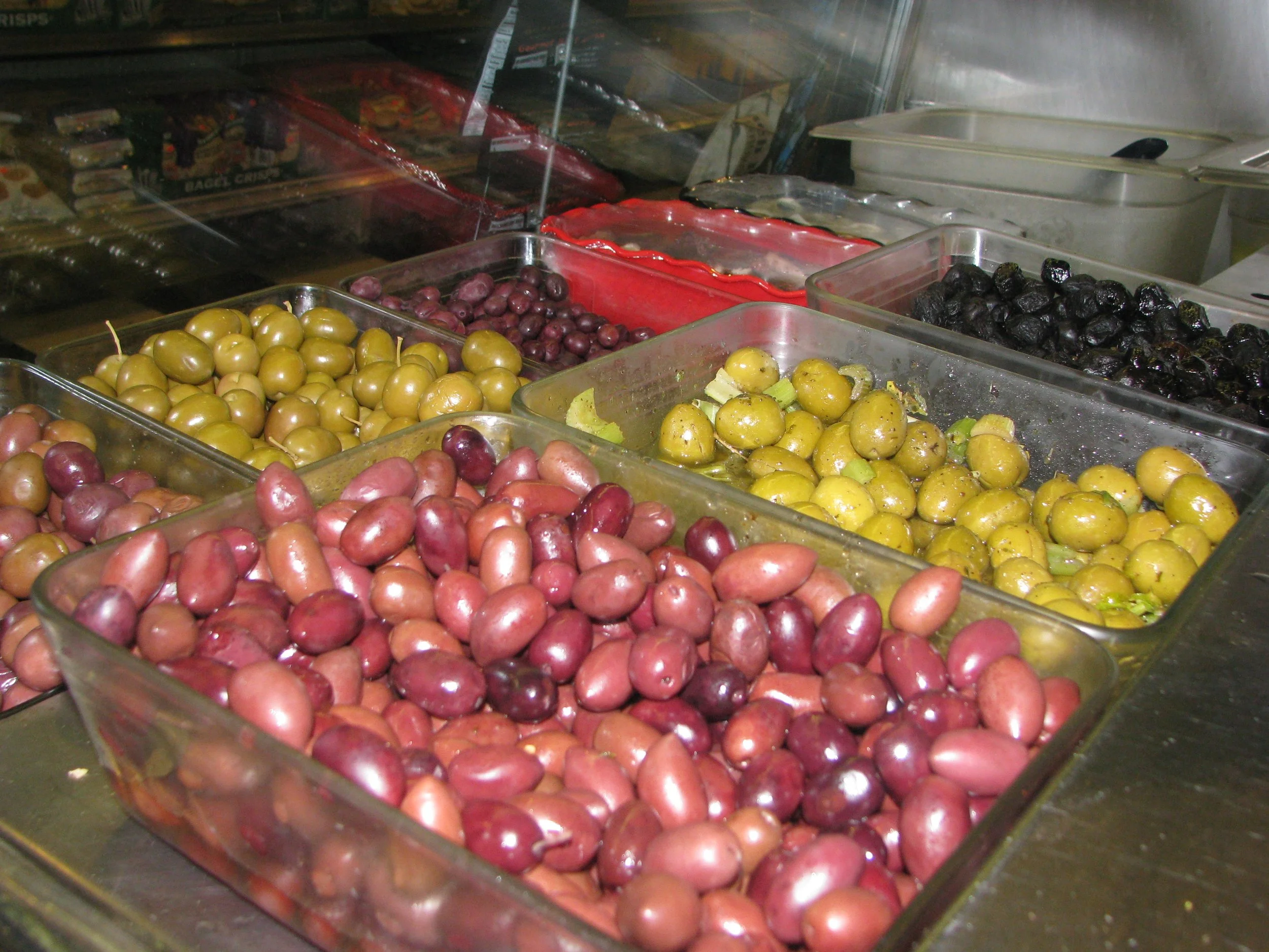 Various jars of pickled olives in different colors, including green, black, and purple, displayed in glass containers.