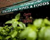 Close-up of green grapes with a store sign in the background reading 'Italian Fine Wines & Foods' and another sign reading 'Come & Taste'.