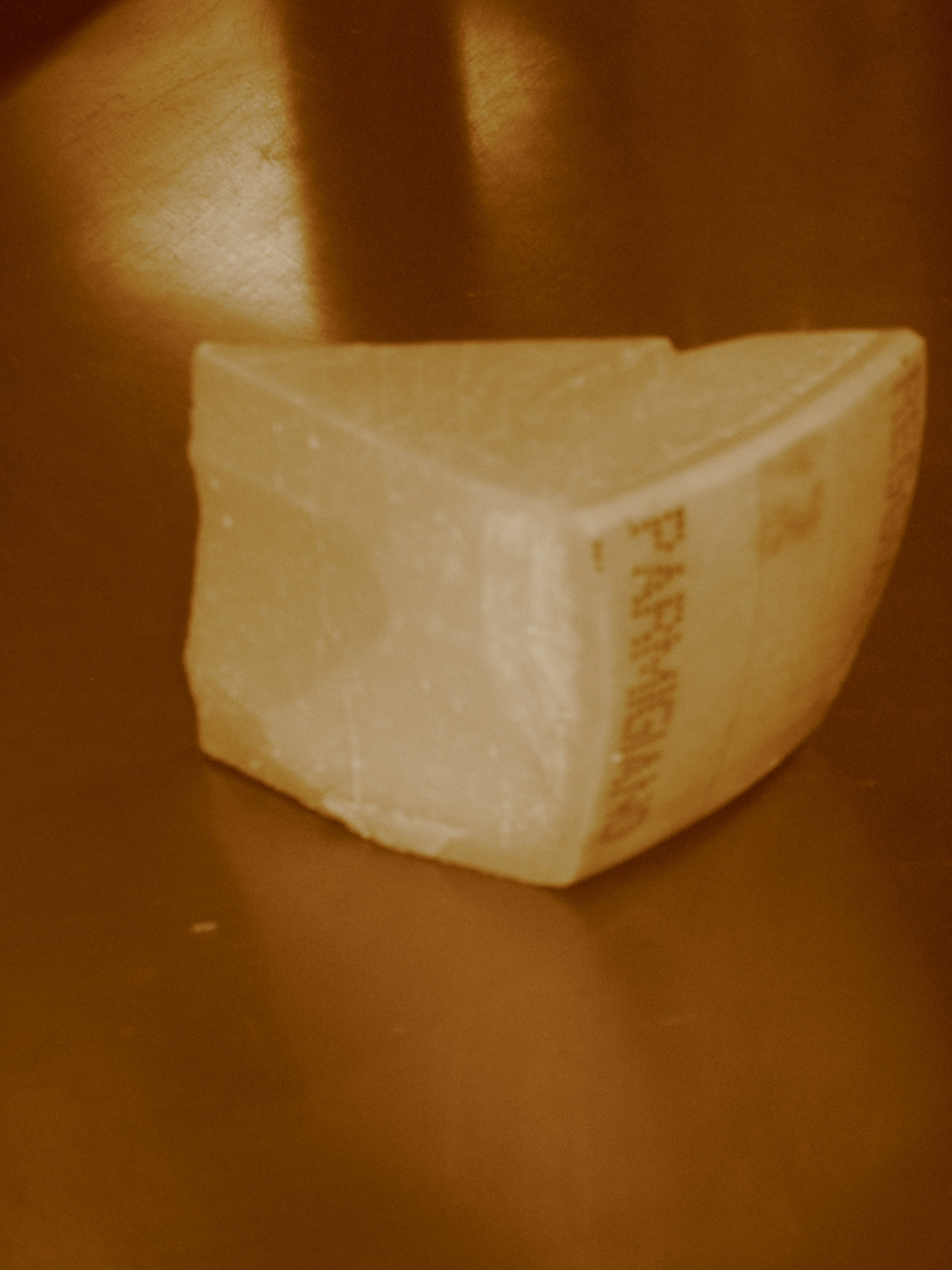 A piece of Parmesan cheese on a gold-colored surface.