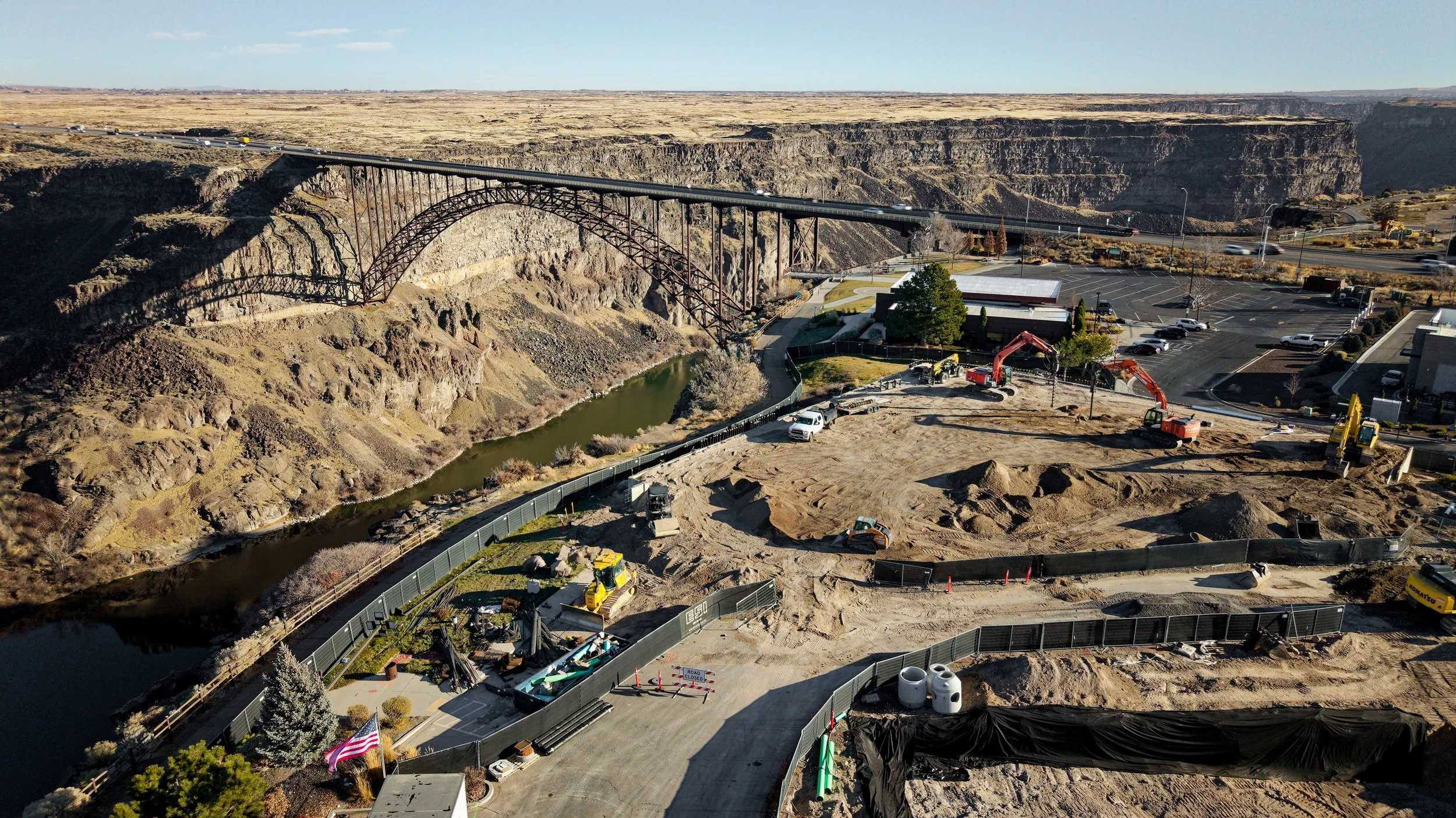 Construction site near a canyon with a bridge, some vehicles, and construction equipment