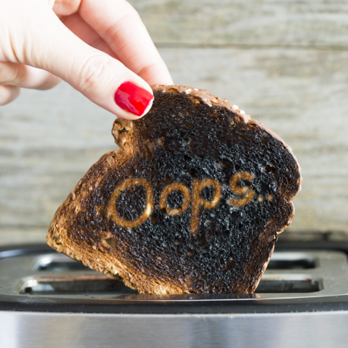 Hand pulls burnt toast from toaster. It has the word "oops" etched into it.