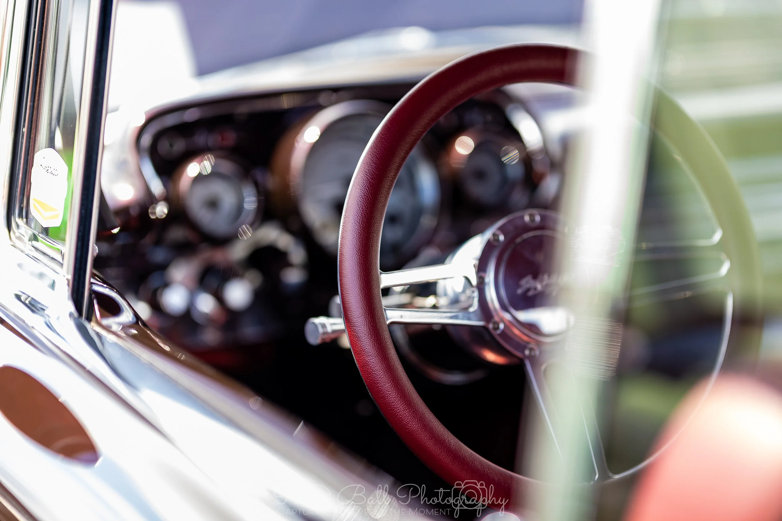 Close-up of a vintage car dashboard and steering wheel with a red cover, with gauges and controls visible behind the wheel.