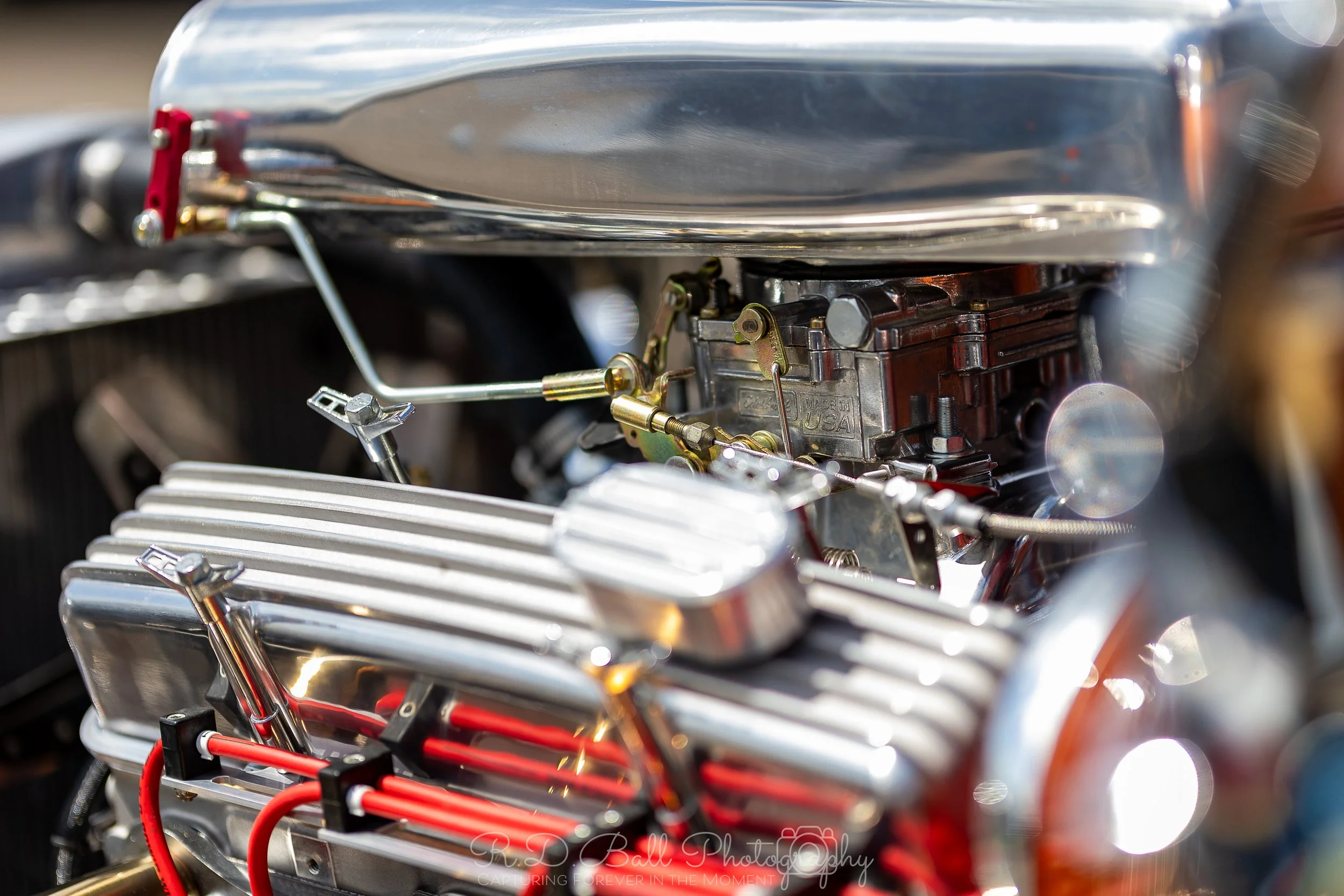 Close-up of a vintage car engine with shiny metal parts, carburetor, and red wiring.