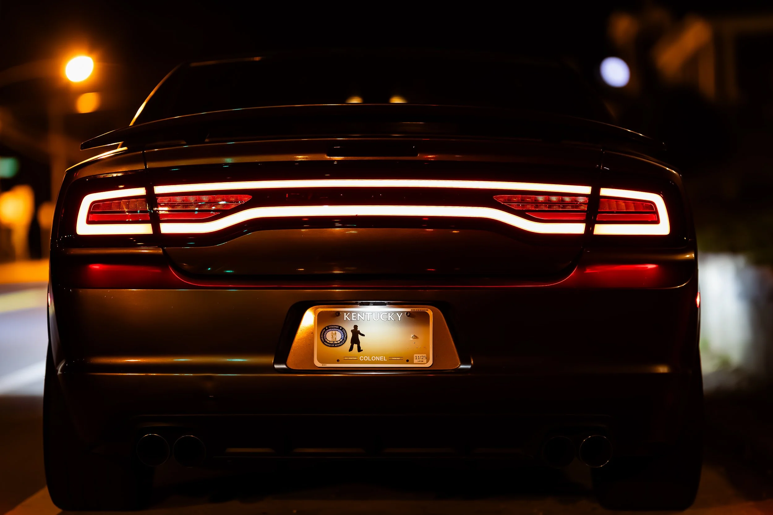 Rear view of a black luxury car with illuminated taillights displaying a distinctive triple-line design parked at night, showing a Kentucky license plate with a silhouette of a golfer.