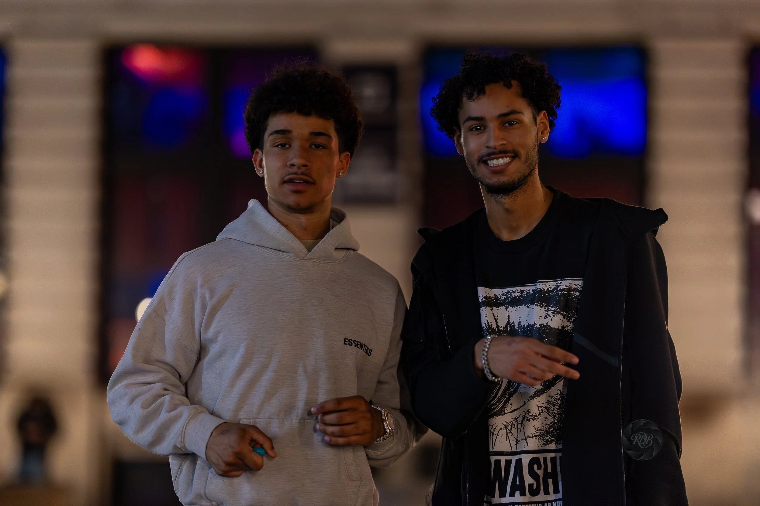 Two young men with curly hair smiling and standing outdoors at night.