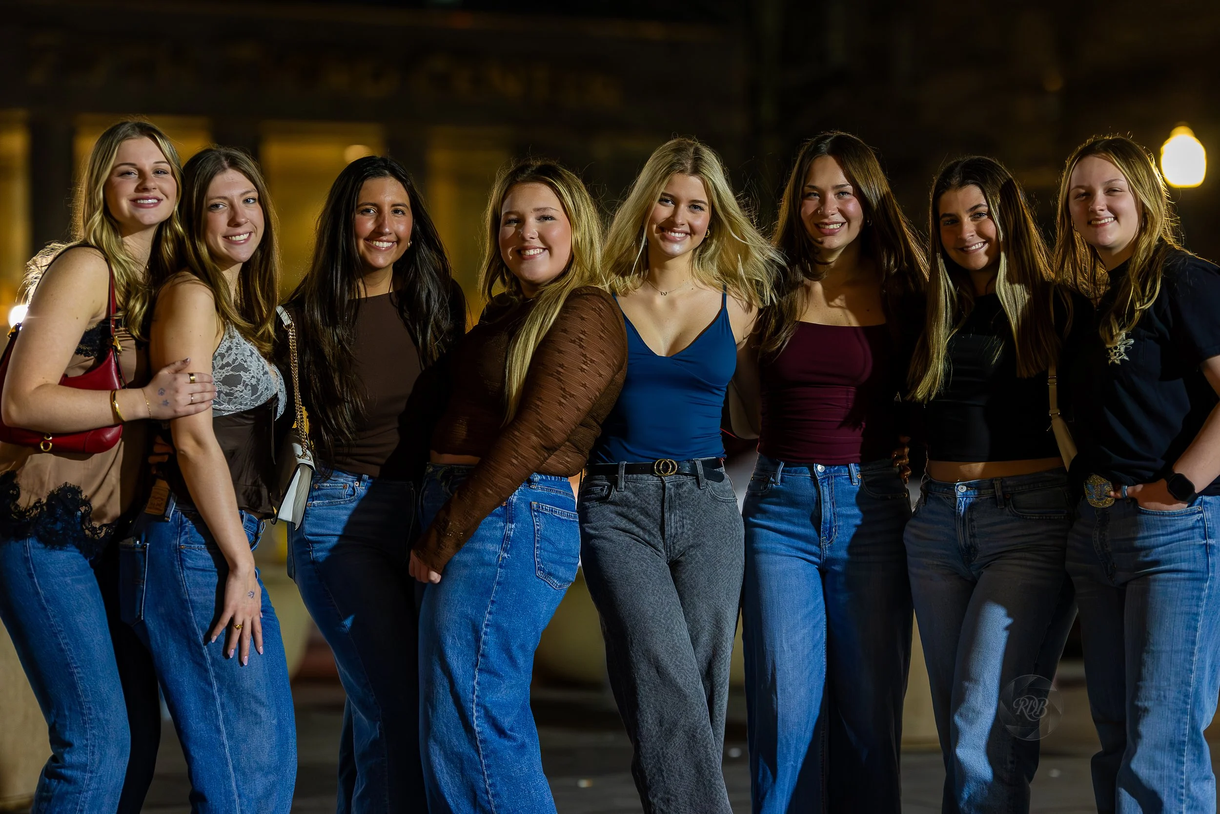 A group of nine young women standing together outdoors at night, smiling for the camera.