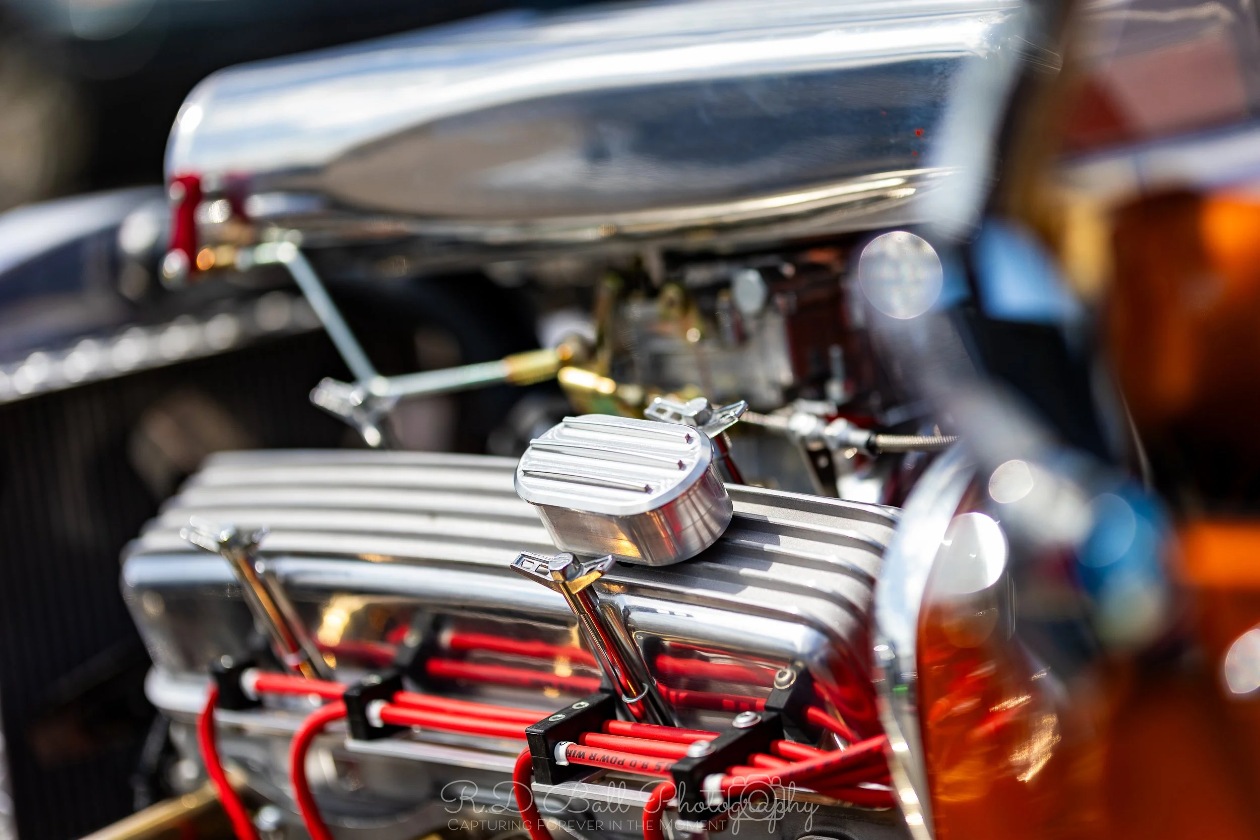 Close-up of a vintage car engine, featuring shiny metallic components, red wires, and a ribbed air filter.