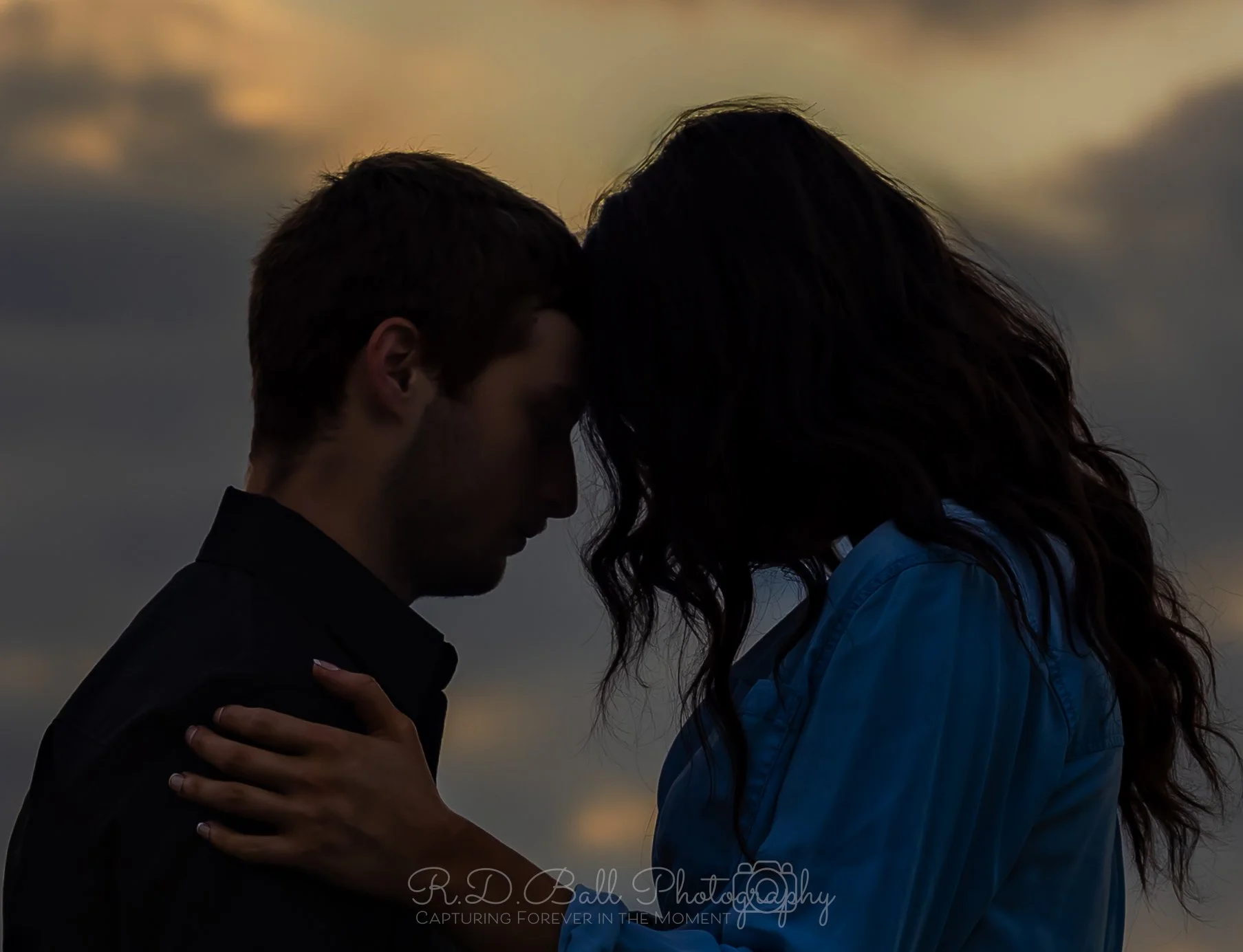 A silhouette of a man and woman facing each other with foreheads touching during sunset.