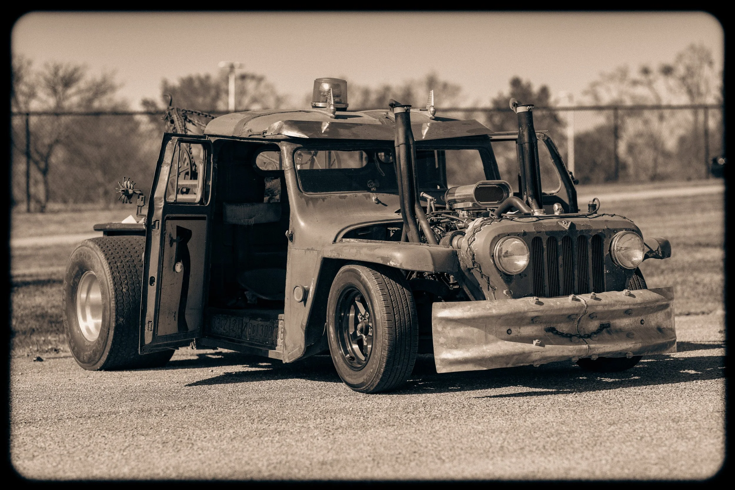 A vintage, heavily modified racing car with a rugged, unfinished look parked on an outdoor track, black and white photo.
