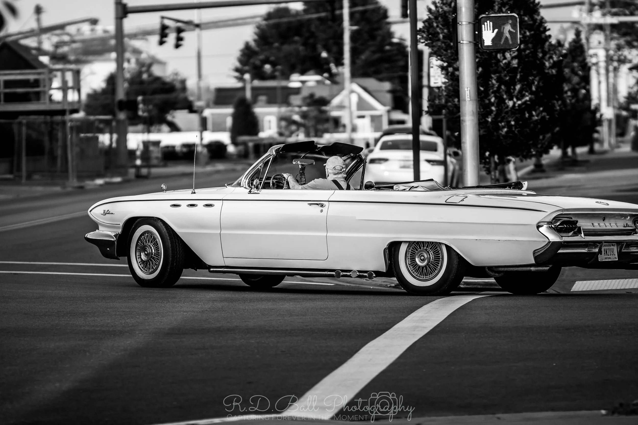 A vintage white convertible car crossing an intersection with a pedestrian crossing signal in the background.