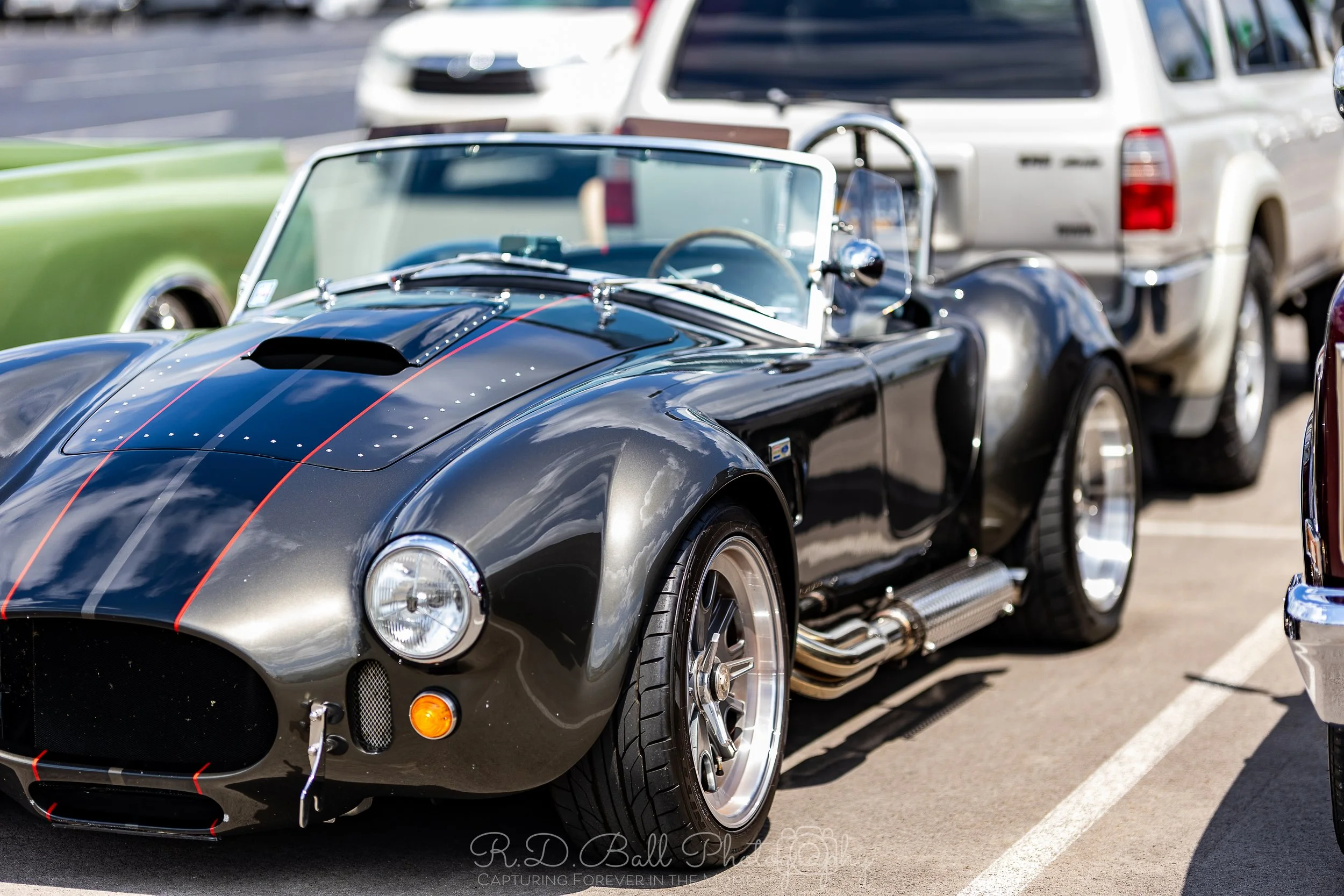 A classic black sports car with red pinstripes parked in a parking lot, surrounded by other vehicles.