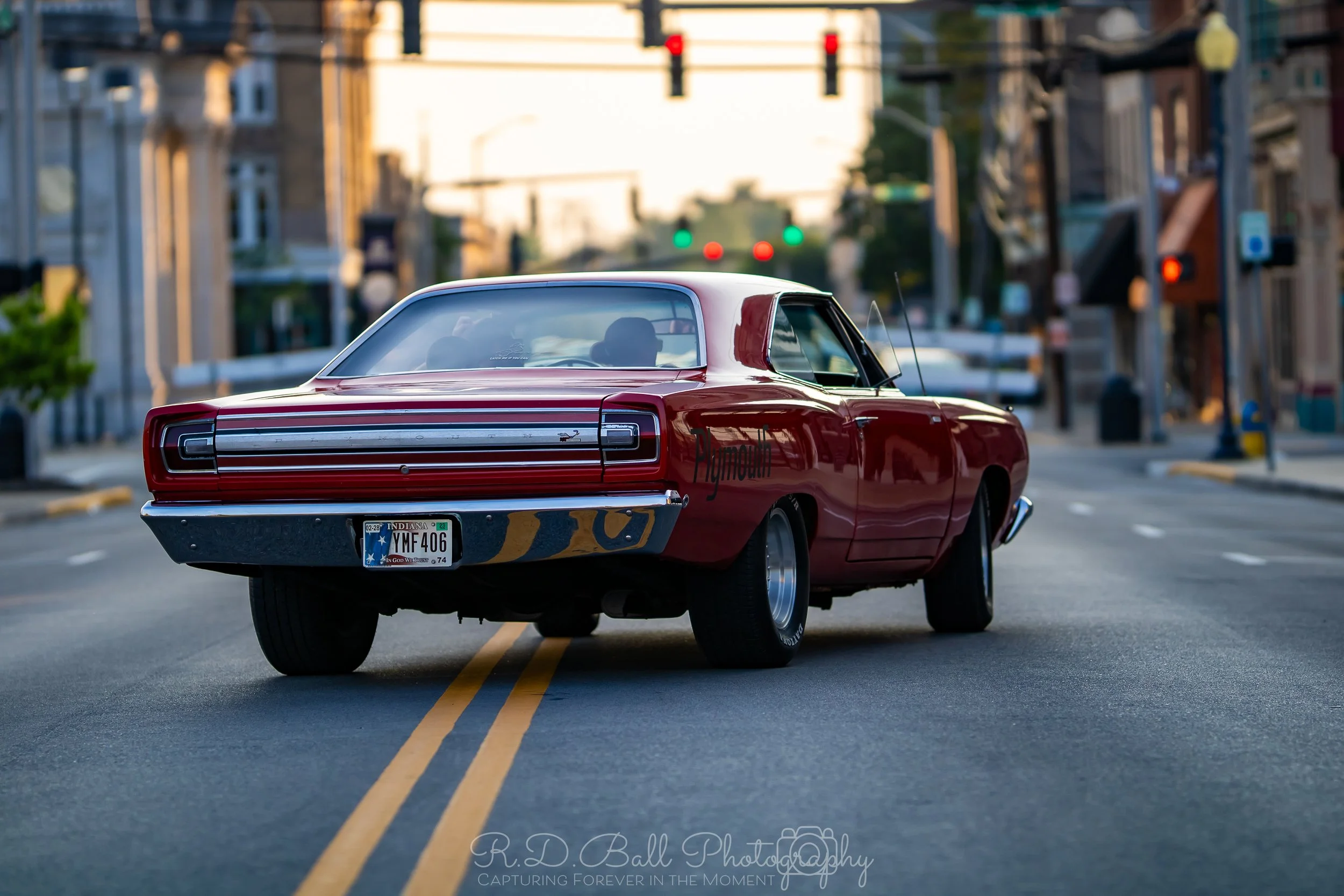 A vintage red Chevrolet car parked on a city street with buildings and traffic lights in the background.