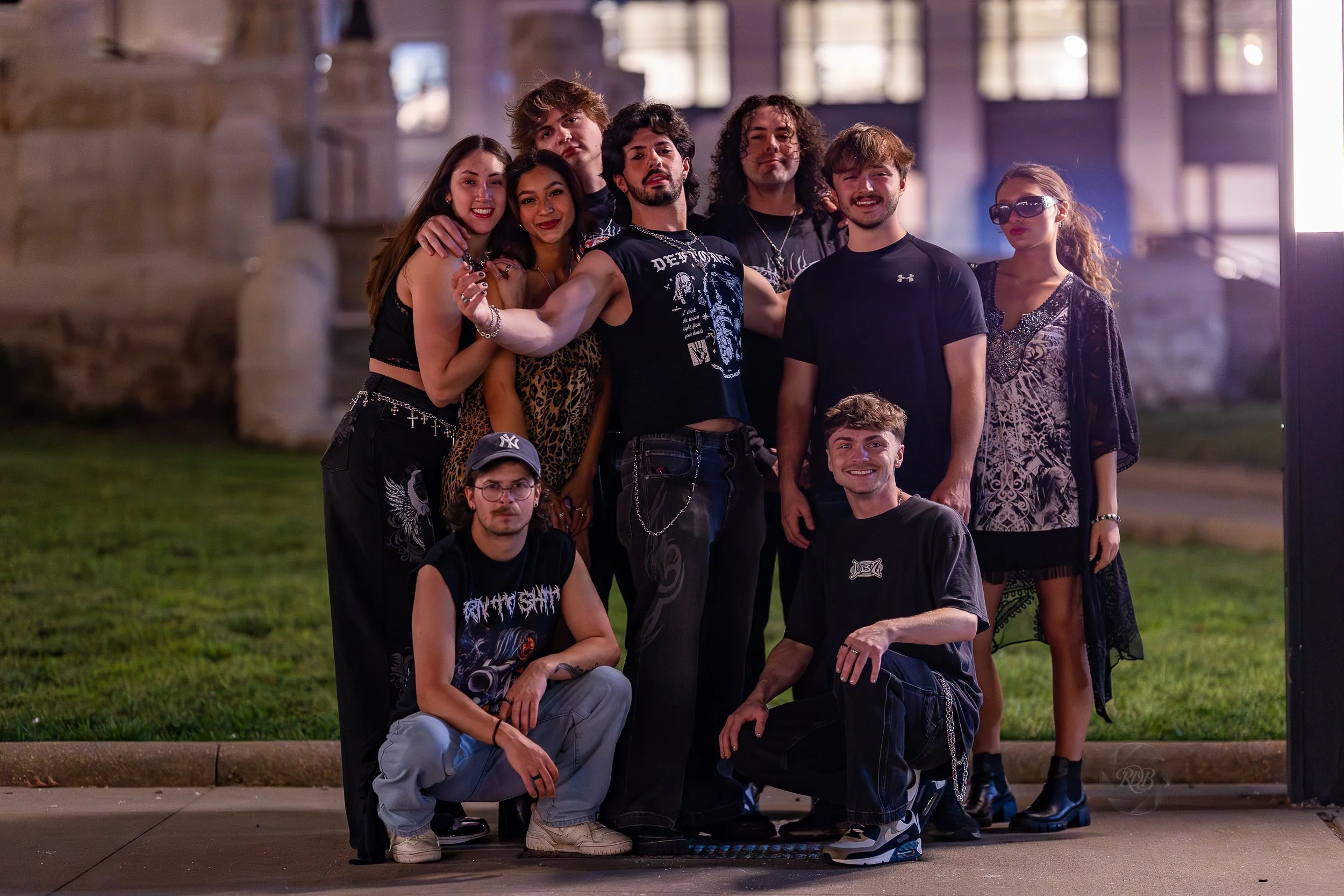 A group of ten young adults posing together outdoors at night in front of a building with large windows