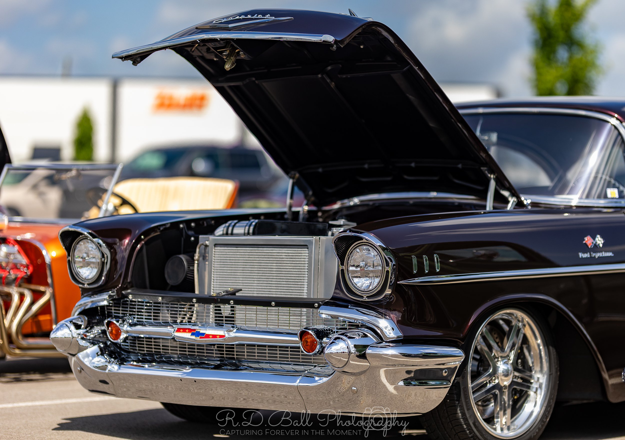 A vintage black Chevrolet car with its hood open on display at a car show, showing the engine compartment and chrome grille.