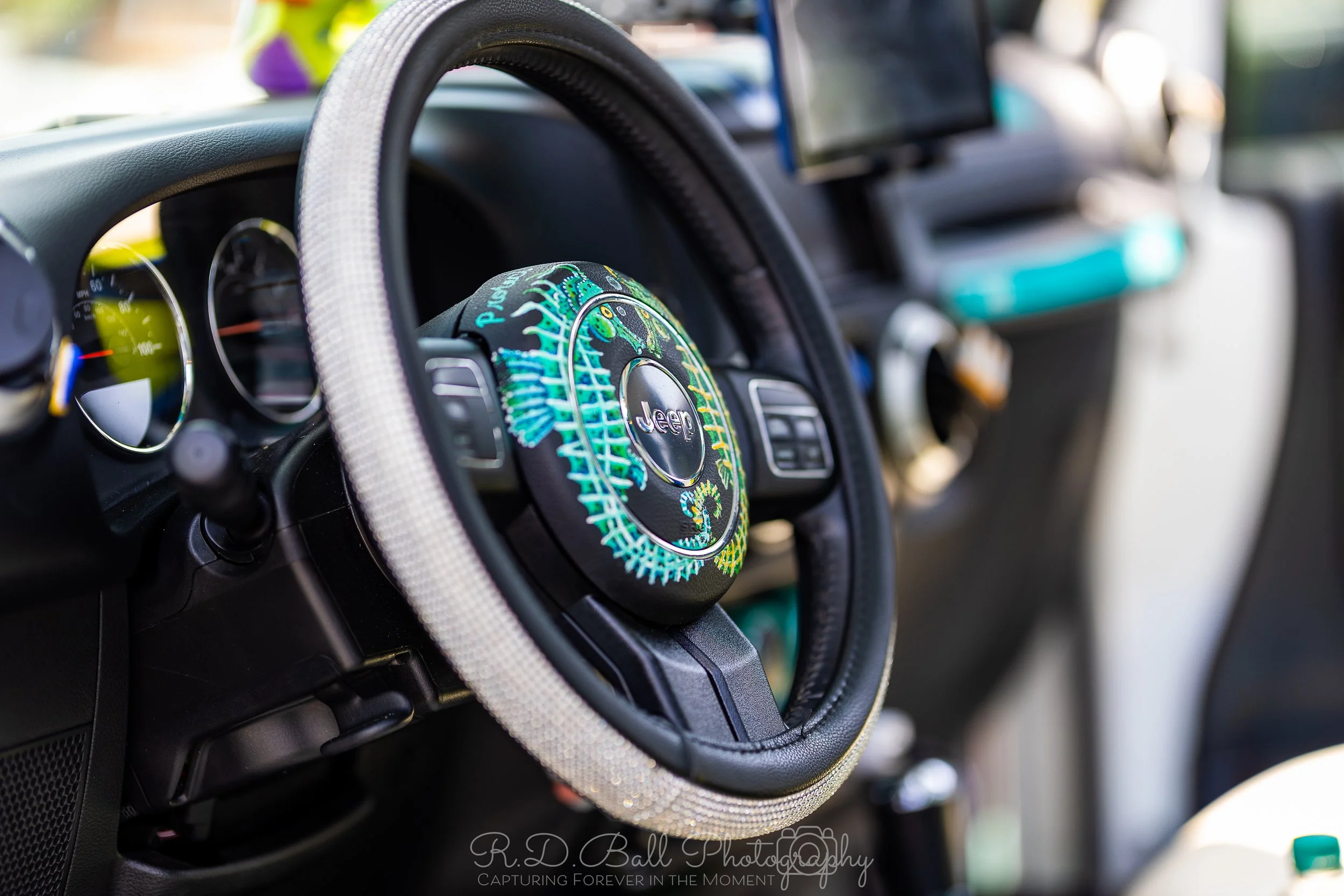 Interior of a Jeep vehicle with a beaded steering wheel cover and a embroidered cover on the steering wheel featuring a dinosaur design.