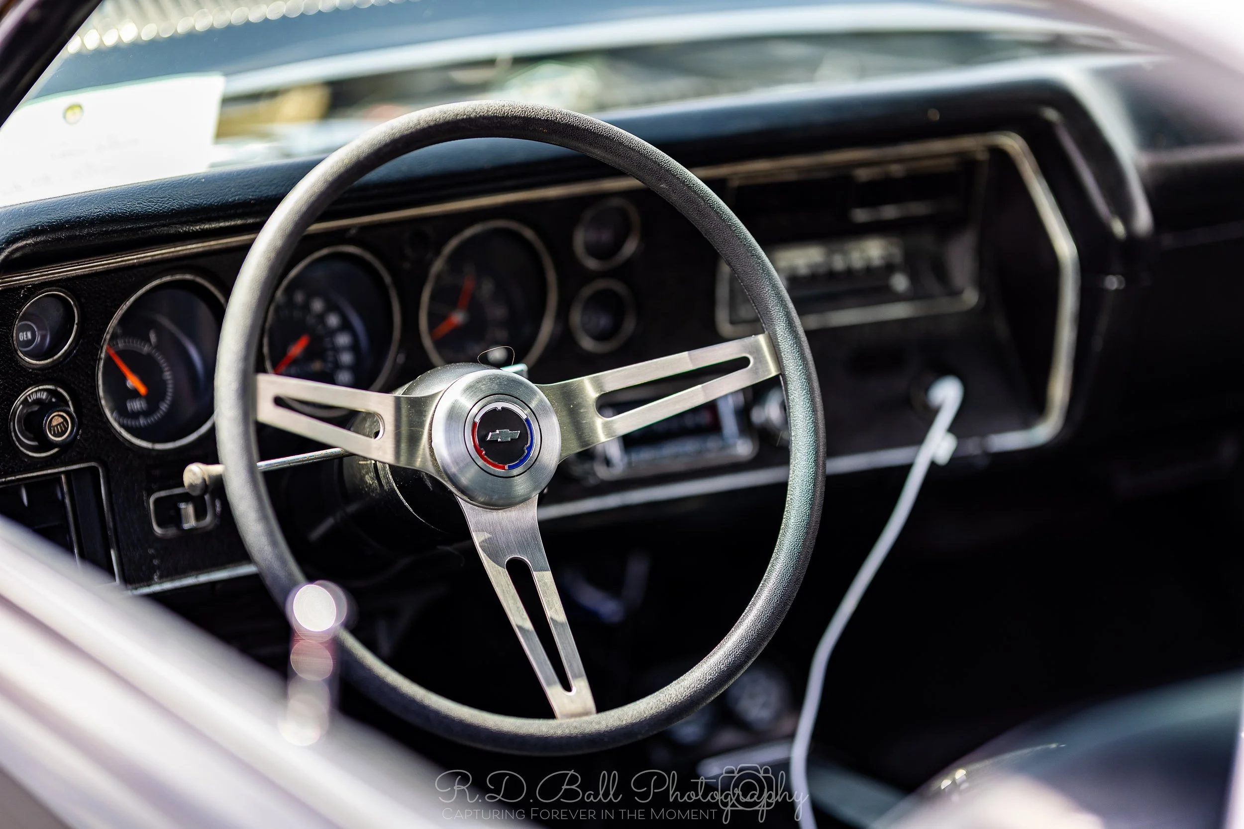 Close-up of a vintage Chevrolet car dashboard showing a steering wheel with Chevrolet logo, analog gauges, and an AM/FM radio.