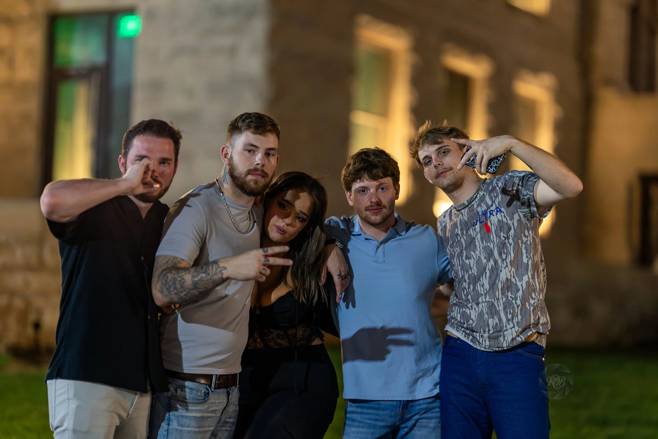 Group of five young adults standing outdoors at night, posing for a photo with a blurred building in the background.