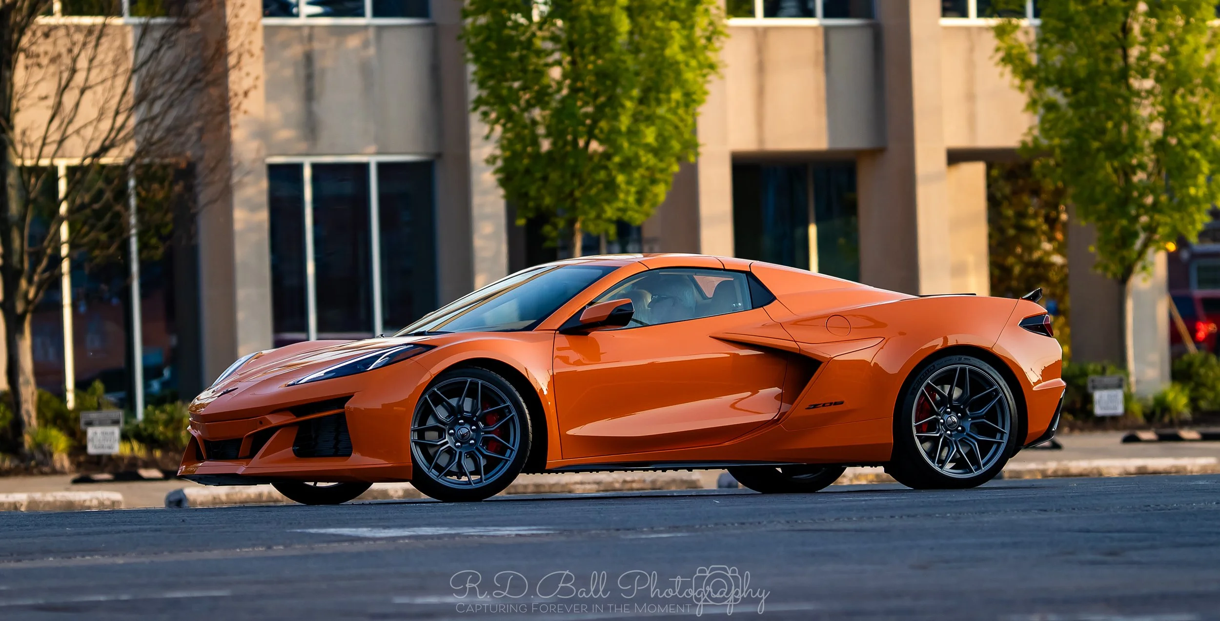 An orange sports car parked on a street in front of a building with trees.