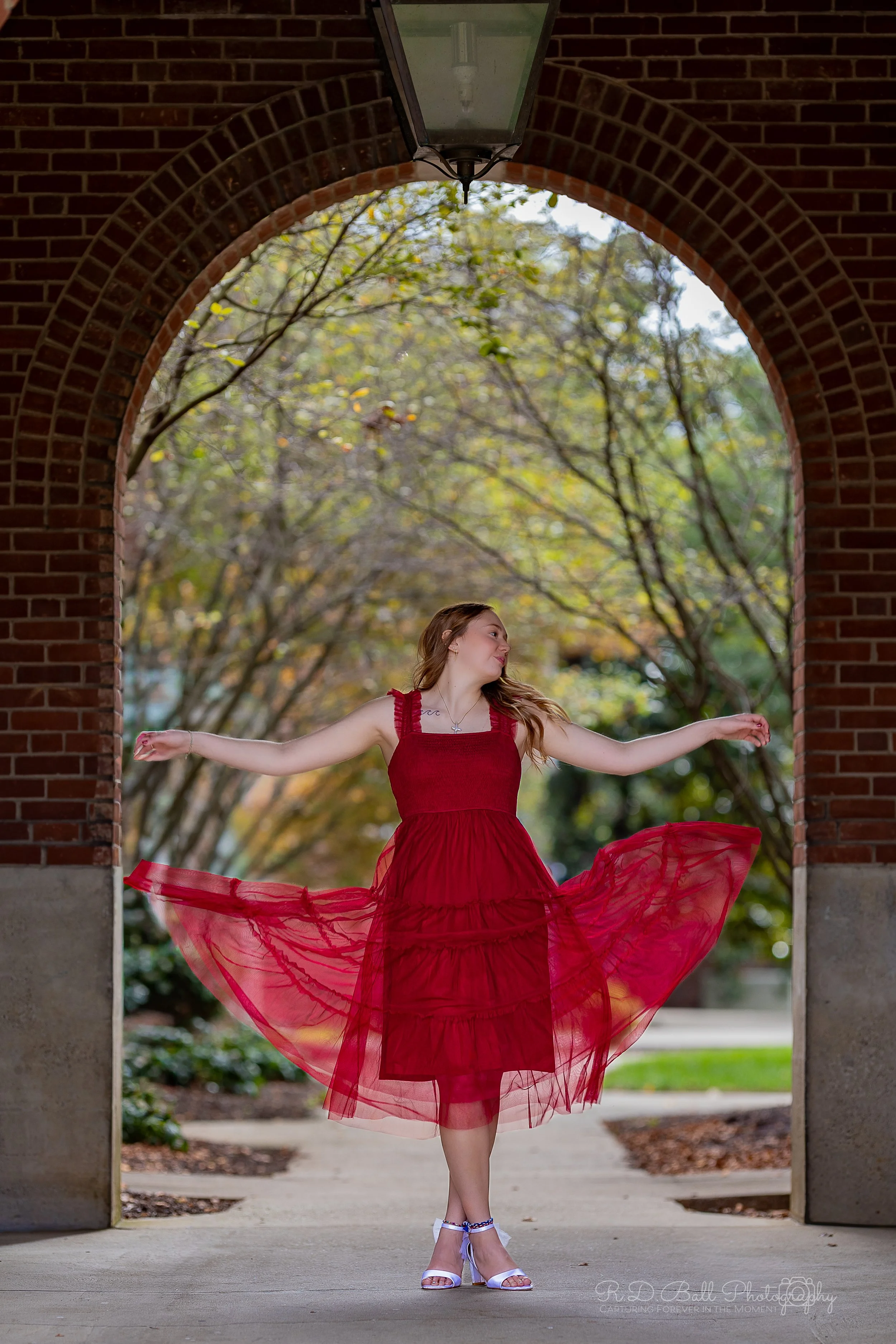 A woman in a red dress twirling under an archway with an outdoor background.