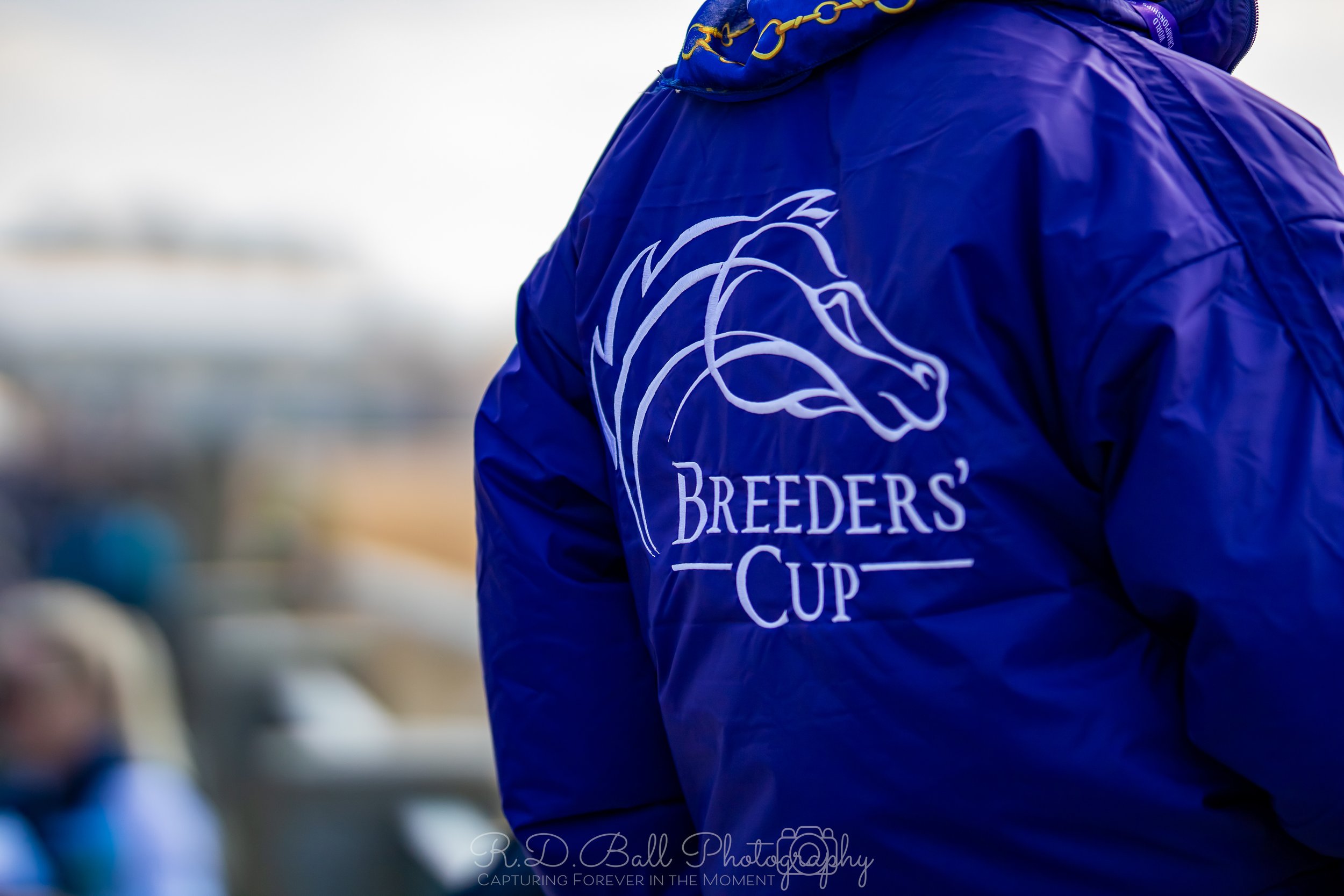 Person wearing a blue jacket with the Breeders' Cup logo on the back, featuring a horse's head outline and the event name.