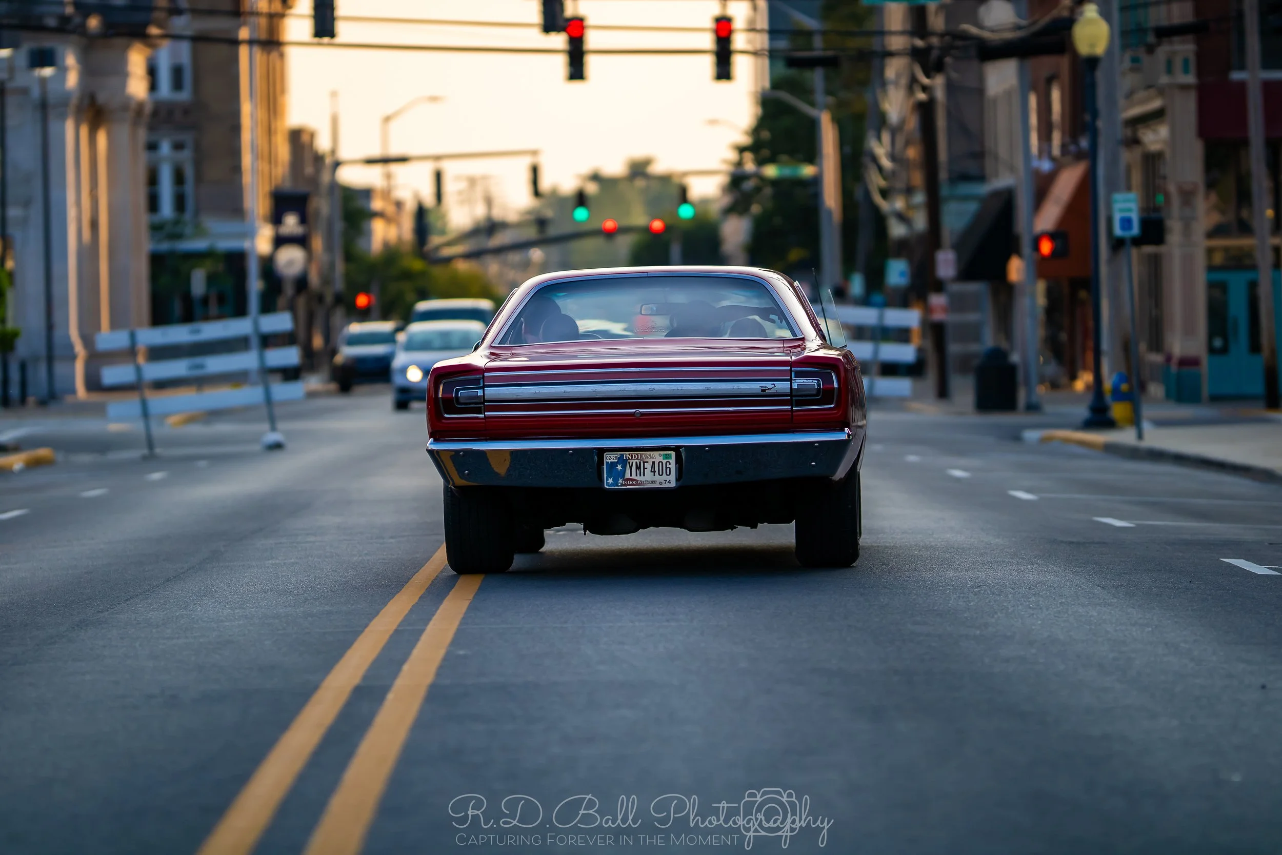 Rear view of a vintage red muscle car stopped in the middle of an urban street at traffic lights during daytime.