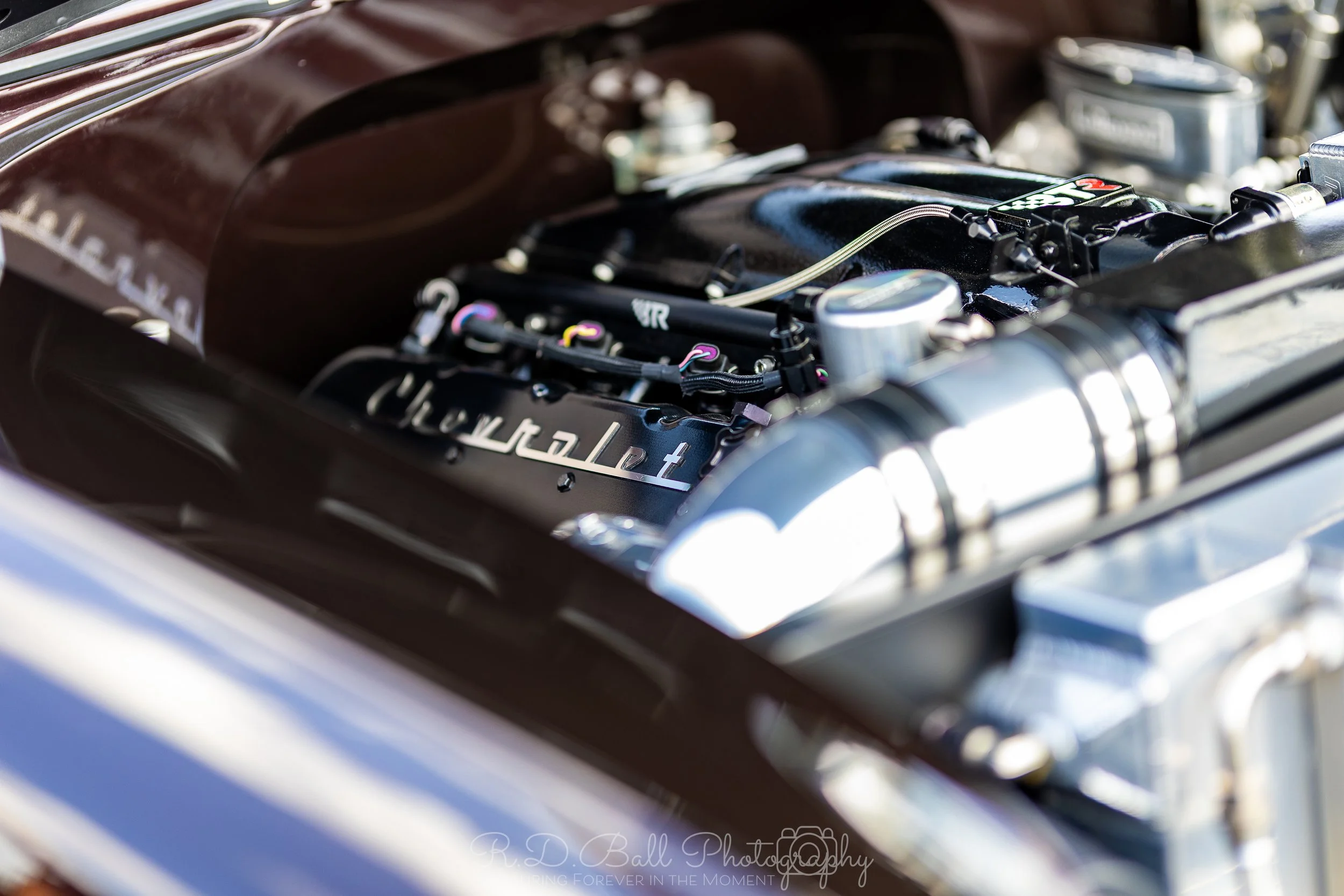 Close-up of a car engine with metal components and wires visible, with part of the car's body in the foreground.